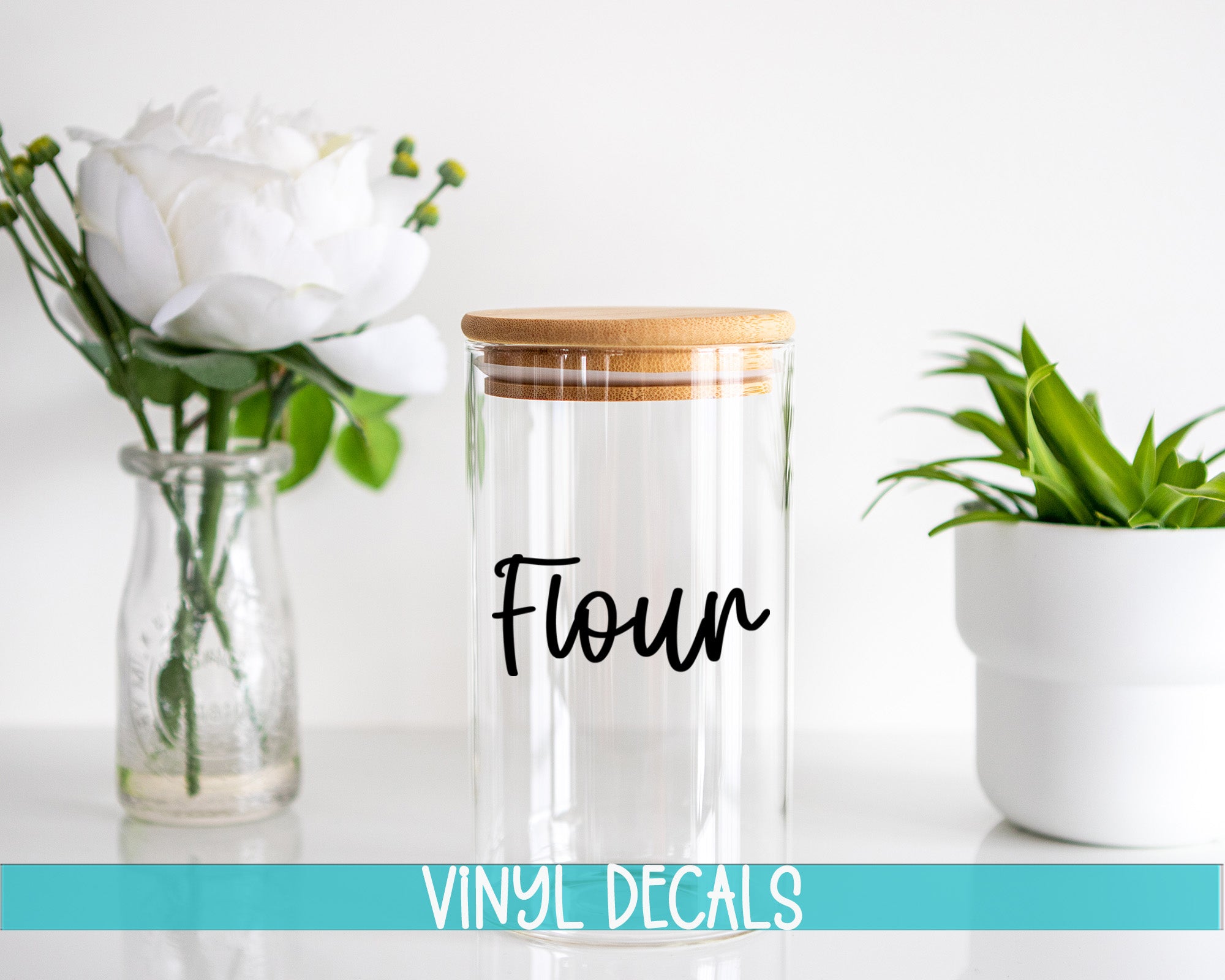 a clear glass jar with a wooden lid, a glass vase with white flowers, and a white pot with a green plant, all placed on a white surface.
