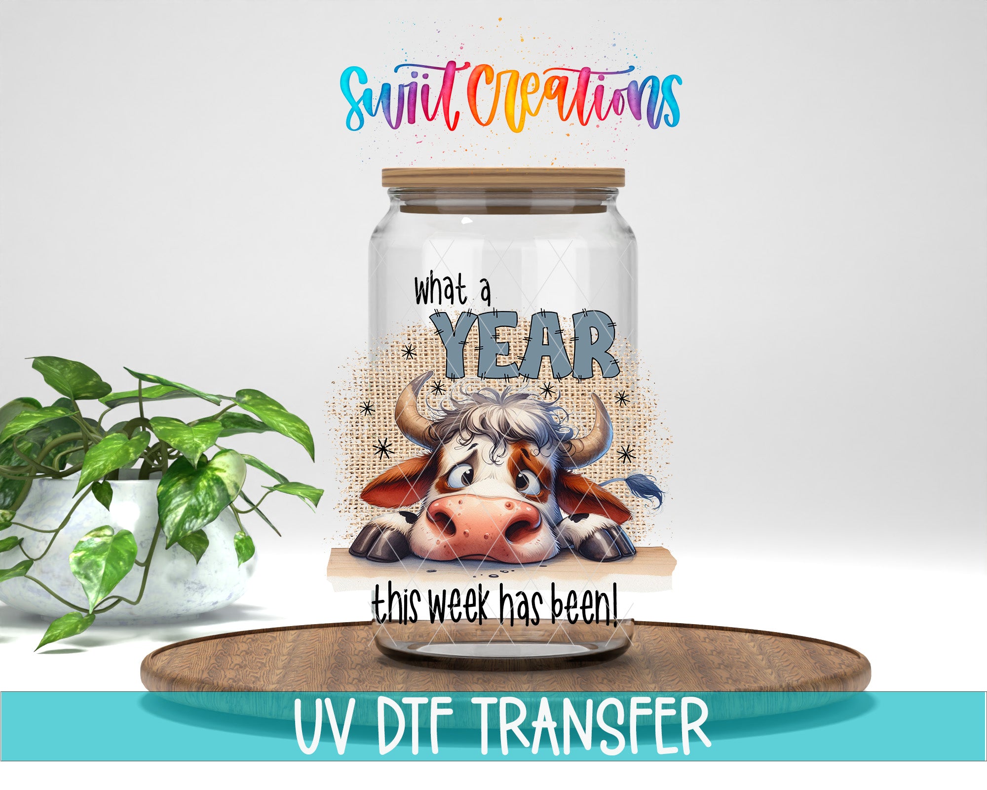 a glass jar with a cartoon cow on it, placed on a wooden surface. The jar has a label that says "What a YEAR this week has been", and there is a plant in the background. The image also includes text that says "UV DFT TRANSFER".