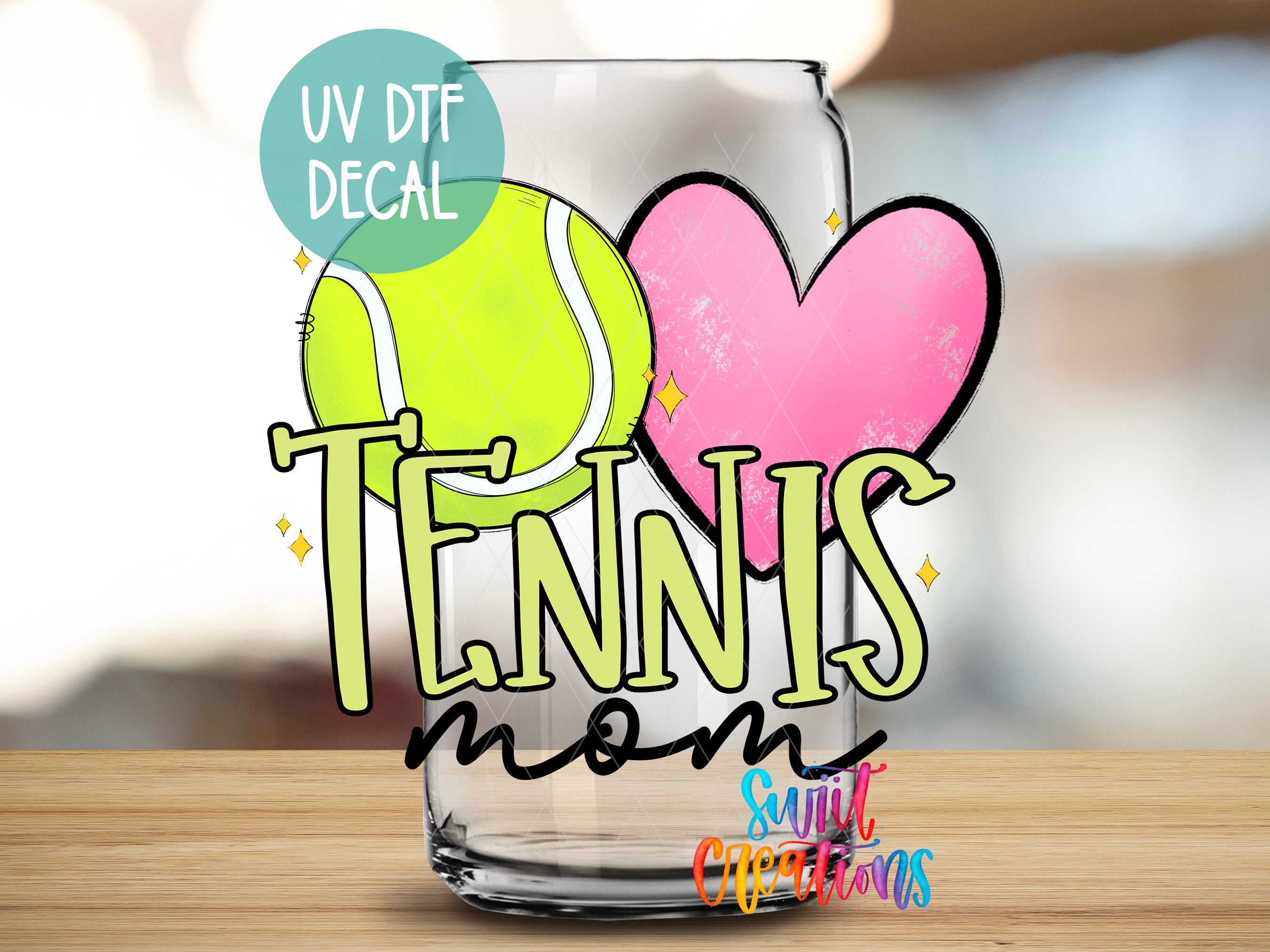 A glass with a tennis ball and a heart, along with the text "TENNIS mom" and "Sunlit Creations" written on it.