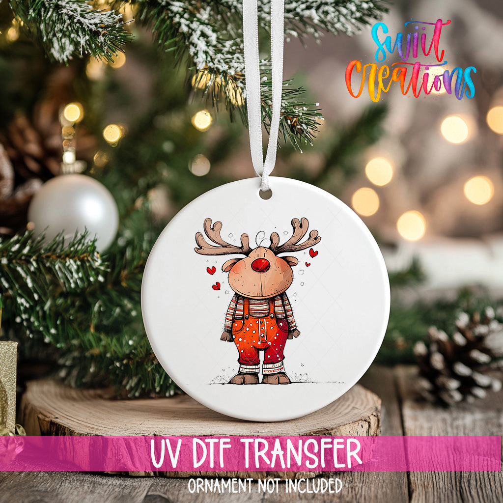 A white ceramic ornament with a cartoon reindeer design hangs on a Christmas tree.