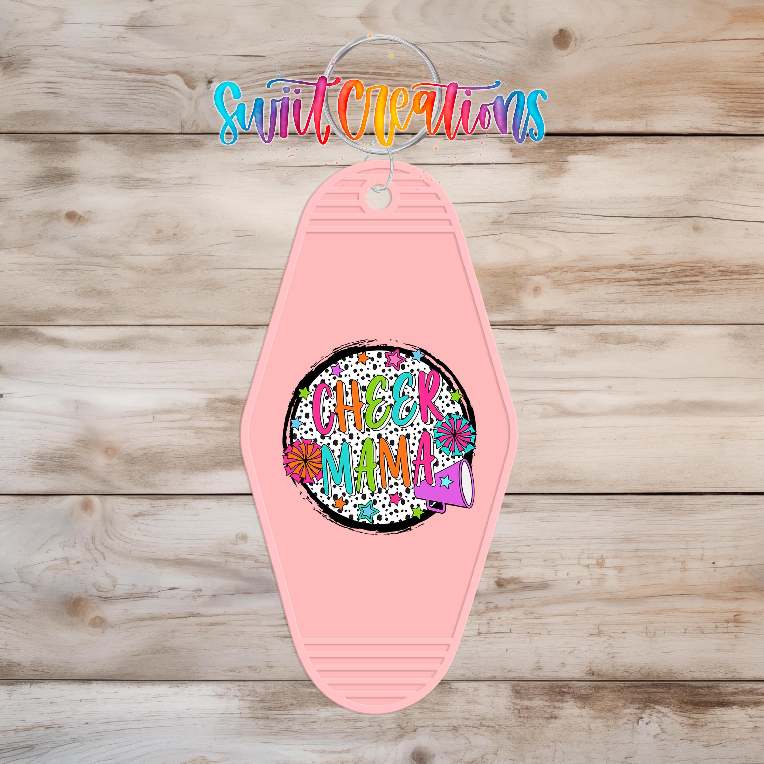 A pink keychain with a colorful, abstract design and text on it, hanging on a wooden surface.