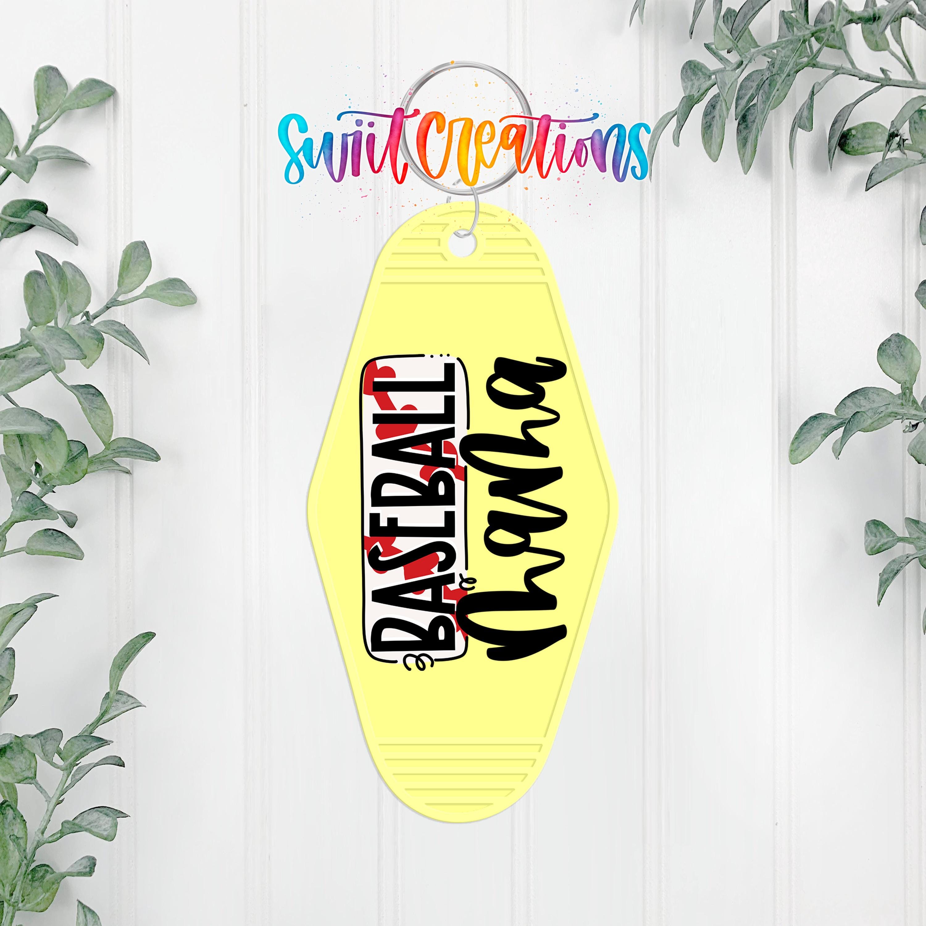 A yellow keychain with the text "Baseball" printed on it, hanging on a white wall with greenery in the background.