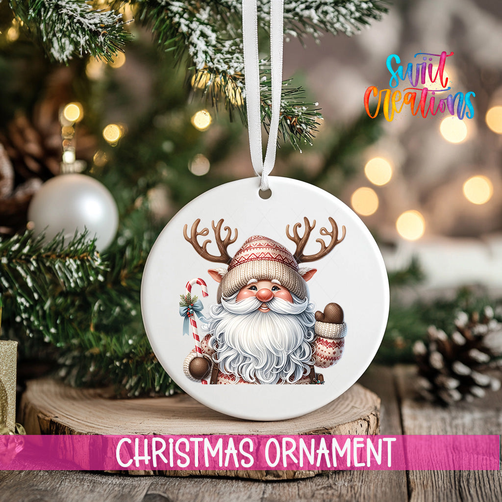 A white Christmas ornament featuring a smiling Santa Claus with antlers is hanging on a tree branch, surrounded by other Christmas decorations and lights.