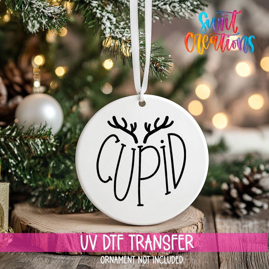 A white ornament with the word "CUPID" written on it, hanging from a Christmas tree.
