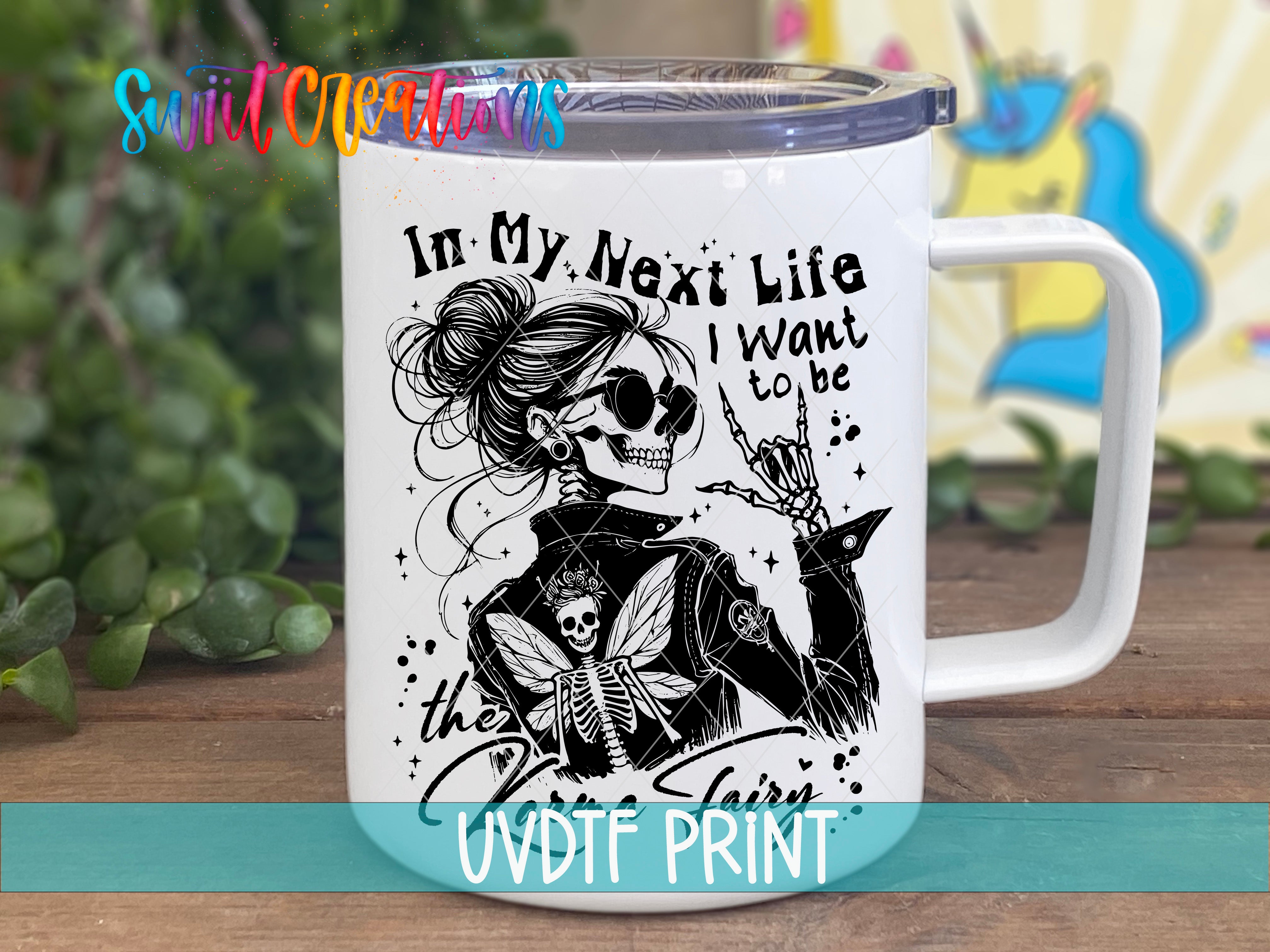 A white mug with a black and white illustration of a skeleton wearing sunglasses and holding a winged creature, accompanied by the text "In My Next Life I Want to be the fairy".