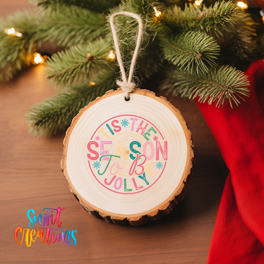 A wooden ornament with a colorful design hangs on a Christmas tree, surrounded by pine branches and twinkling lights.
