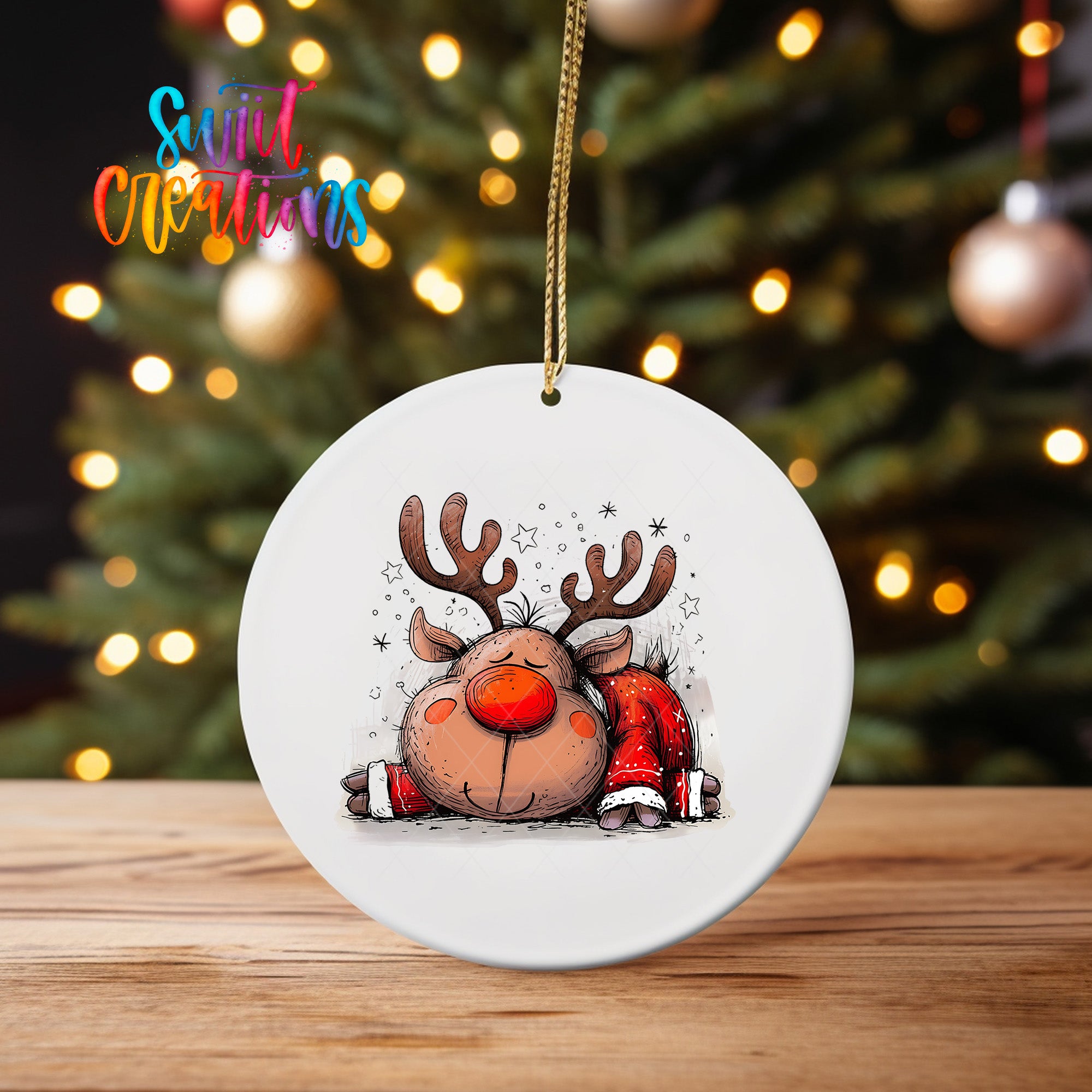 A white ceramic ornament featuring a cartoon reindeer with antlers and a red nose, sitting on a wooden surface in front of a blurred Christmas tree with twinkling lights.