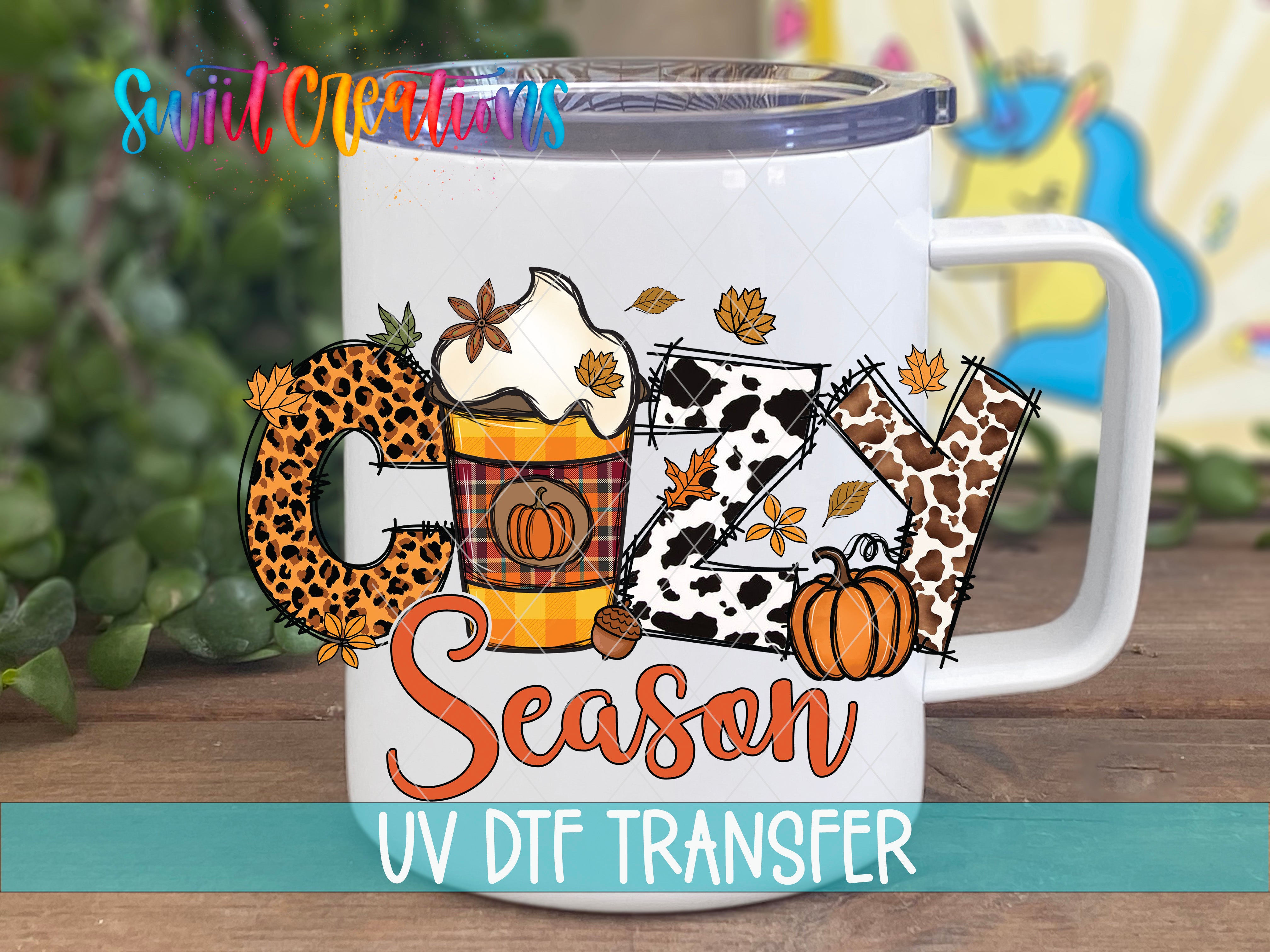 A white mug with a colorful design featuring the word "COZY" and various fall-themed elements such as leaves, pumpkins, and a leopard print pattern.