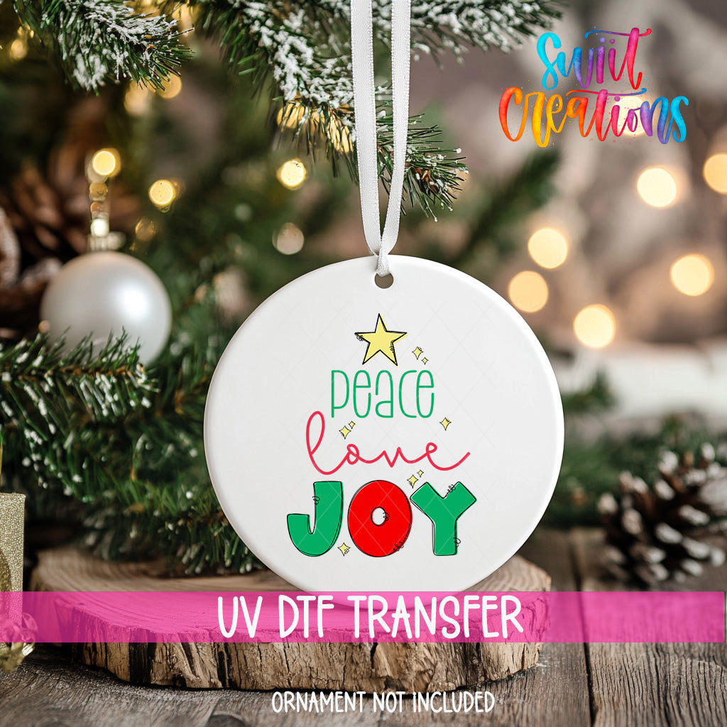 A white ornament with a message of peace and joy hanging on a Christmas tree.