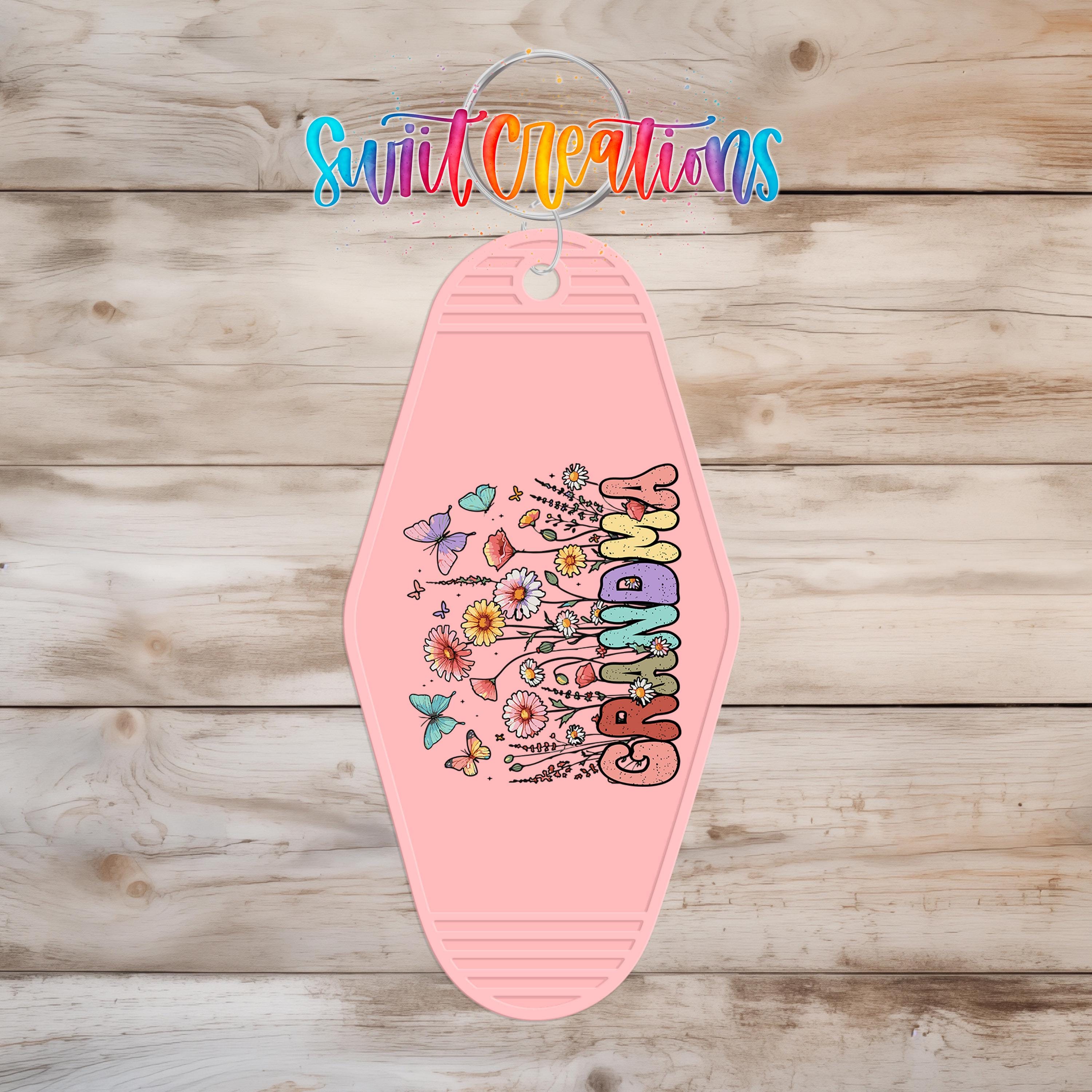 A pink keychain with a floral design and the word "GRANDMA" printed on it, hanging on a wooden surface.