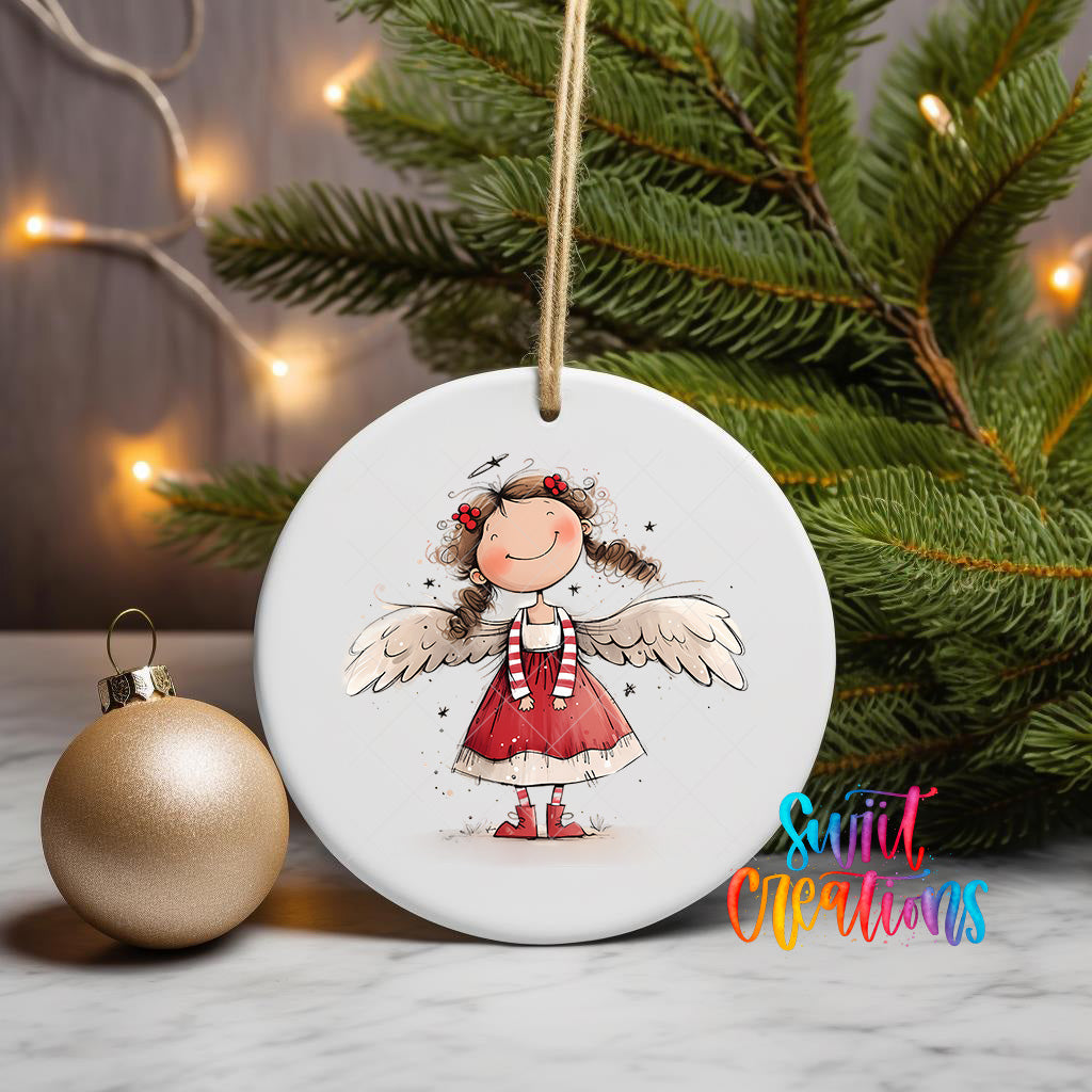 A white ceramic ornament featuring a smiling girl with wings, surrounded by Christmas lights and a gold ornament on a marble surface.