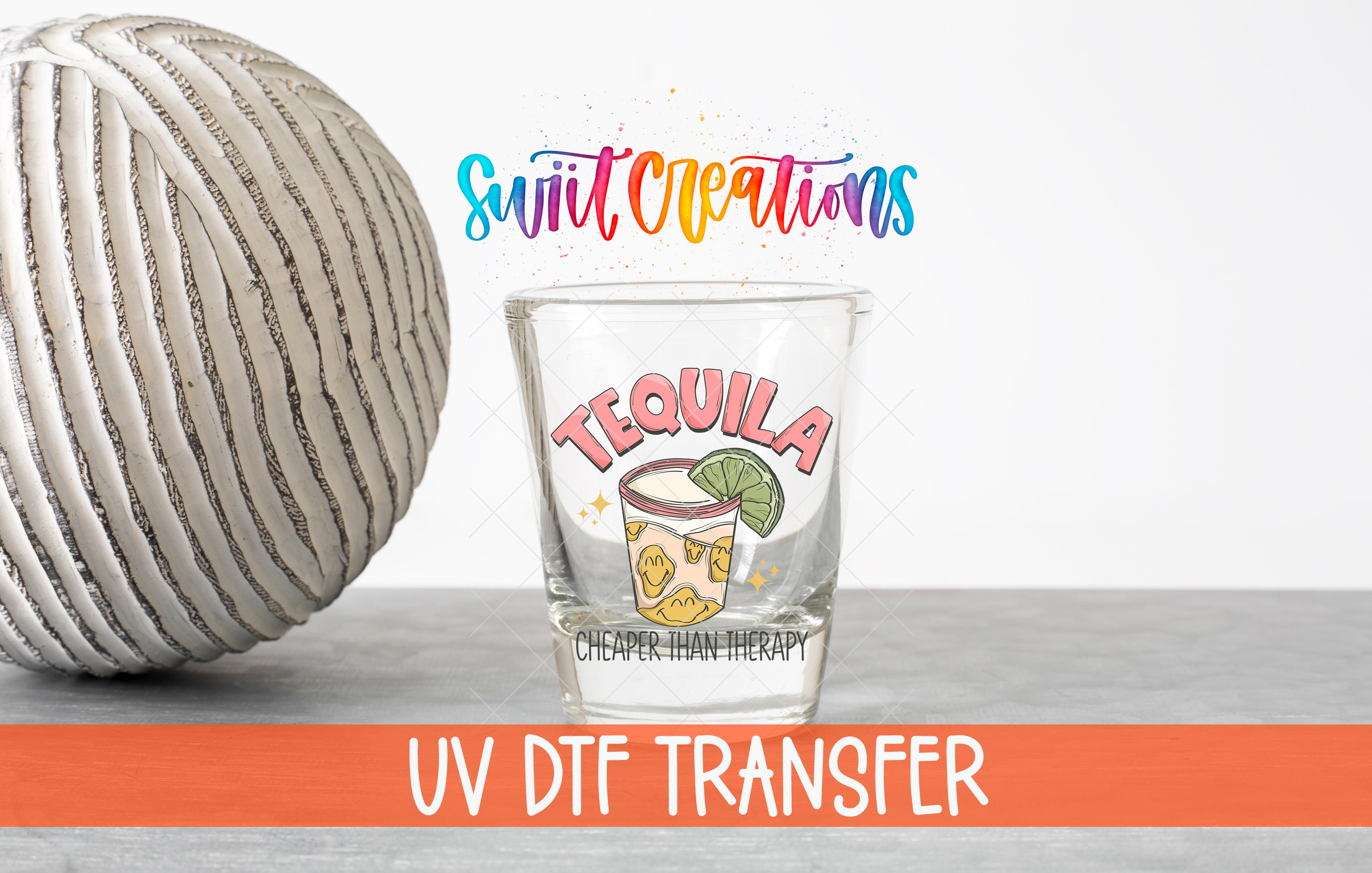 a clear shot glass with a tequila-themed design, placed on a gray surface next to a gray and white striped ball. The shot glass has a colorful design and text that reads "TEQUILA" and "CHEAPER TAN THERAPY". The image also includes text that says "UV DFT TRANSFER" and "LESS THAN 500 CHARACTERS".
