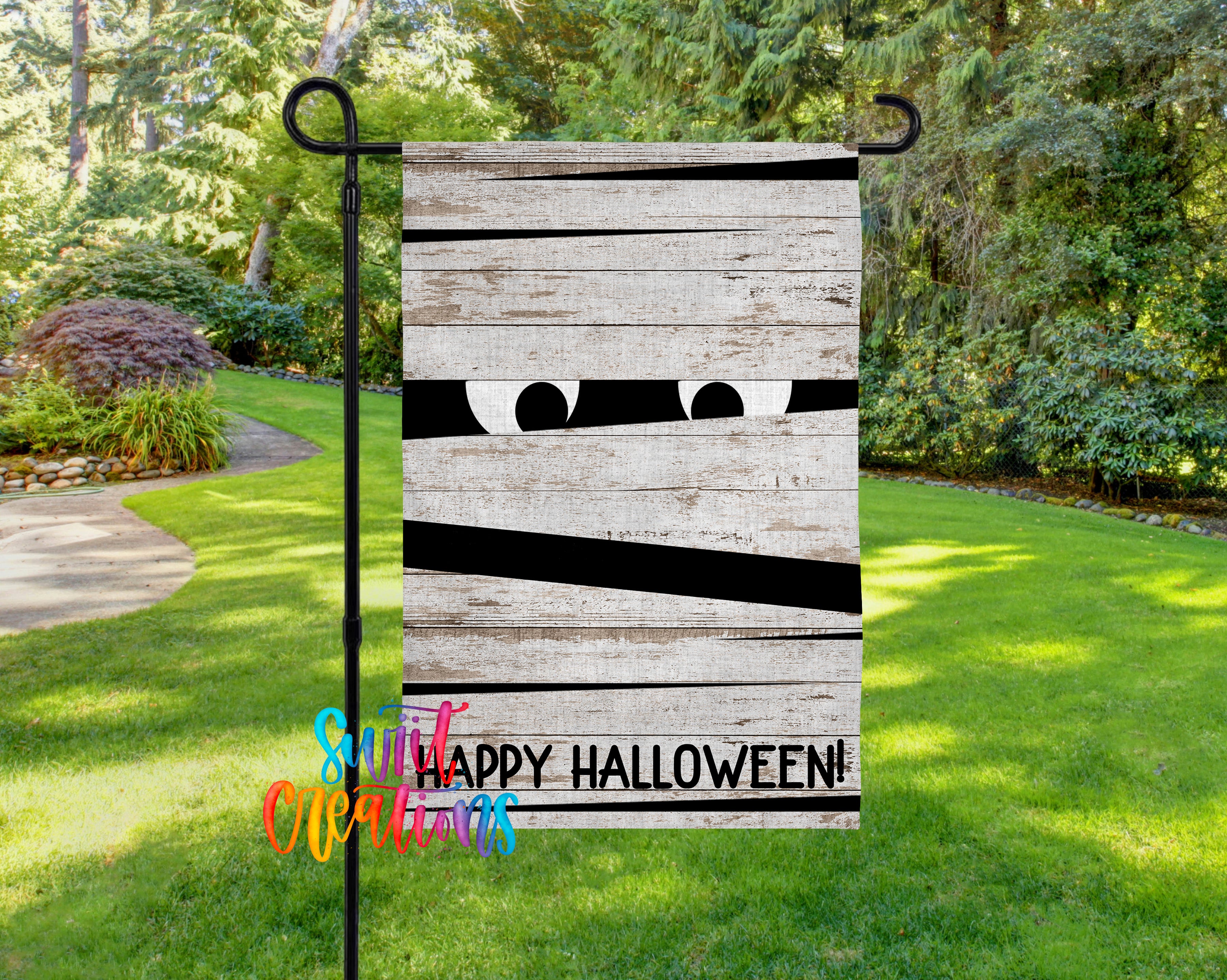 A garden flag with a wooden board design and a pair of eyes peeking out from behind it, set against a backdrop of lush greenery and a path.