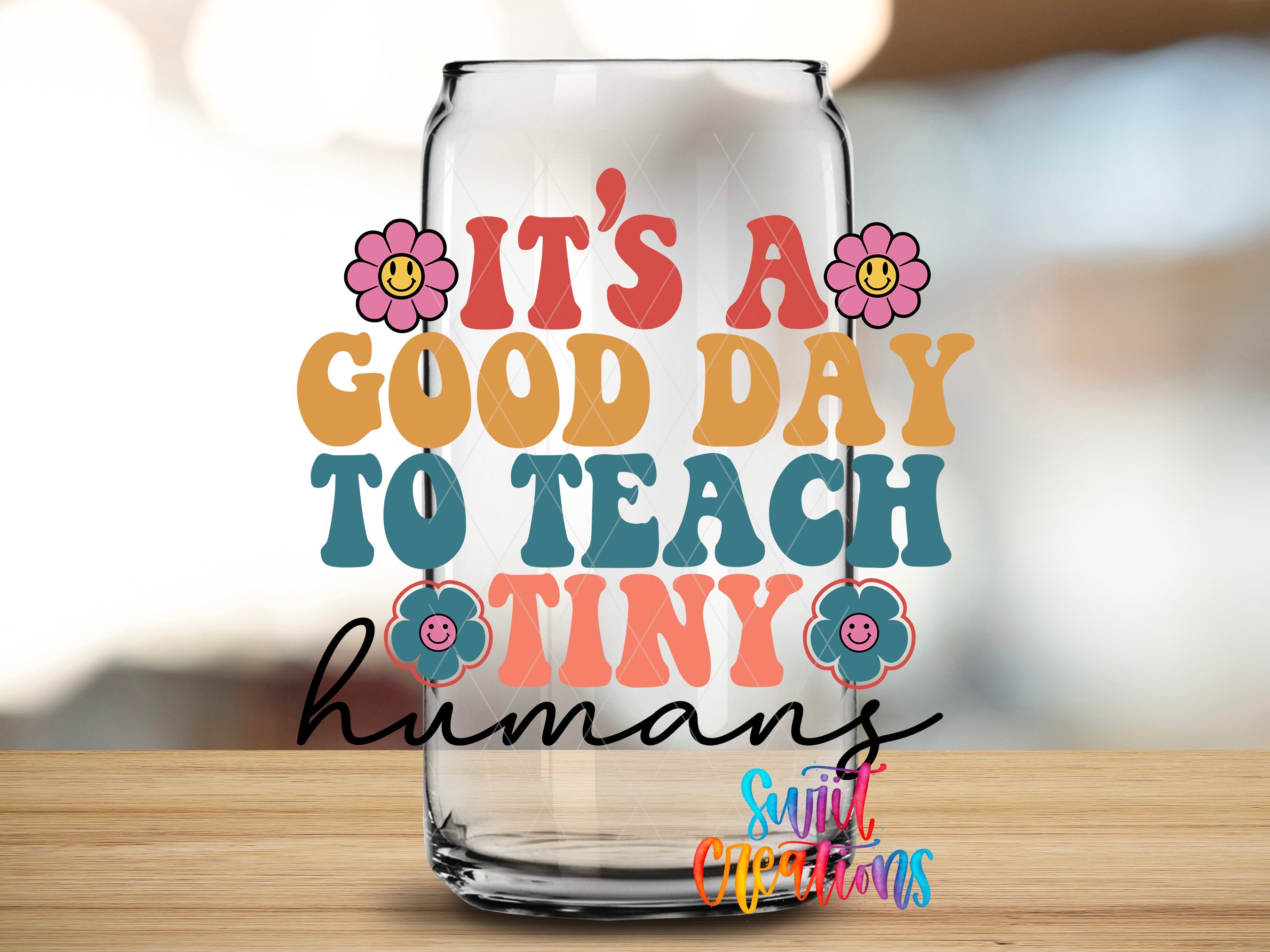 A clear glass jar with a colorful design and text that reads "IT'S A GOOD DAY TO TEACH Tiny humans" and "Sunt Creations" written on it.