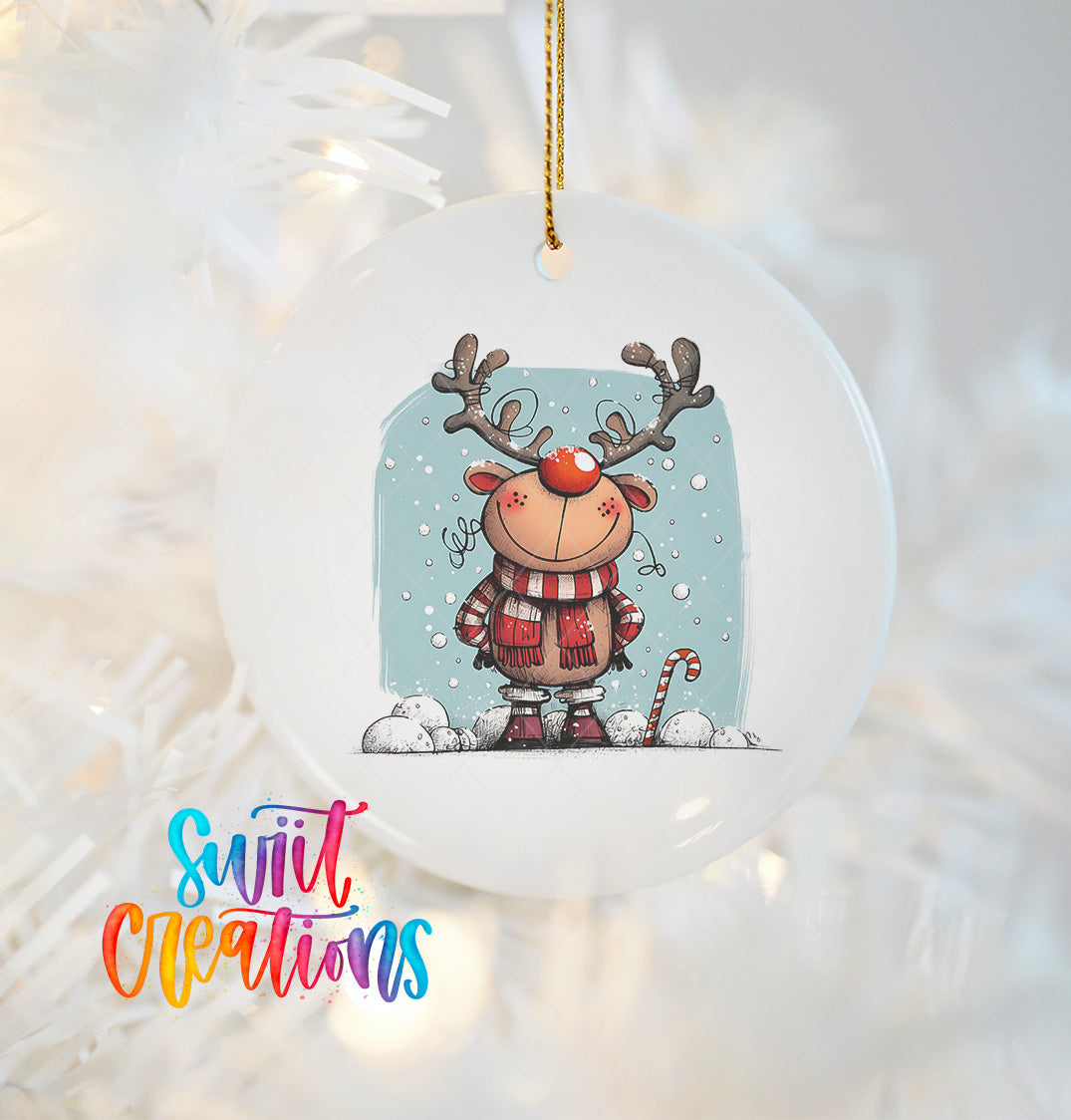 A white ornament featuring a cartoon reindeer with antlers and a scarf, hanging on a Christmas tree.