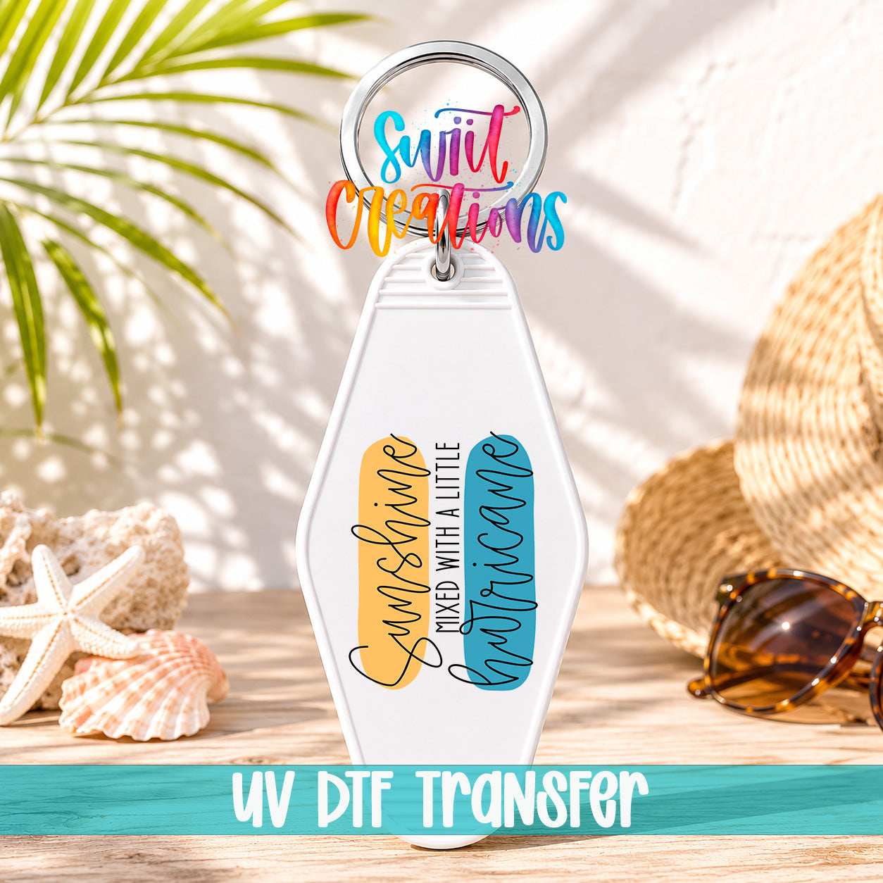 A keychain with a colorful design and text, placed on a wooden surface with sunglasses, a straw hat, and a palm frond in the background.