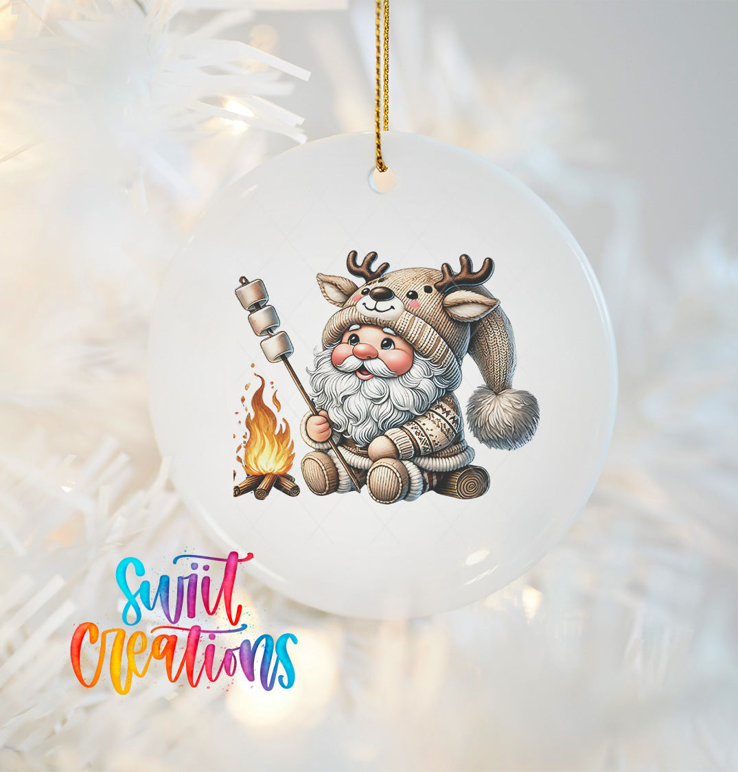 A white ornament featuring a cartoon Santa Claus character with antlers, holding a marshmallow over a campfire.