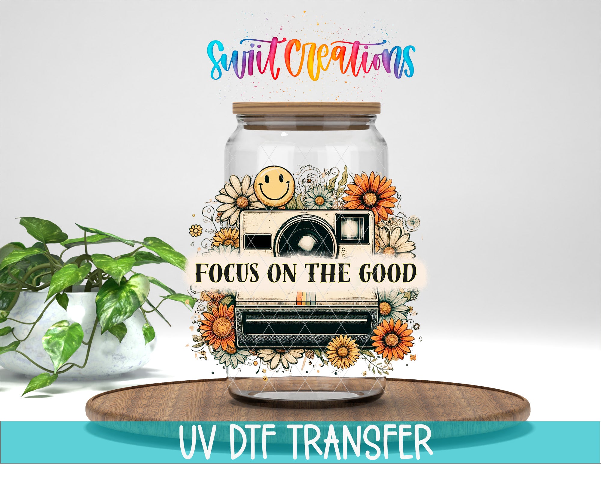 a glass jar with a camera and flowers, along with the text "Focus on the good" and "Swift Creations" written above it. The jar is placed on a wooden surface, and there is a potted plant in the background.
