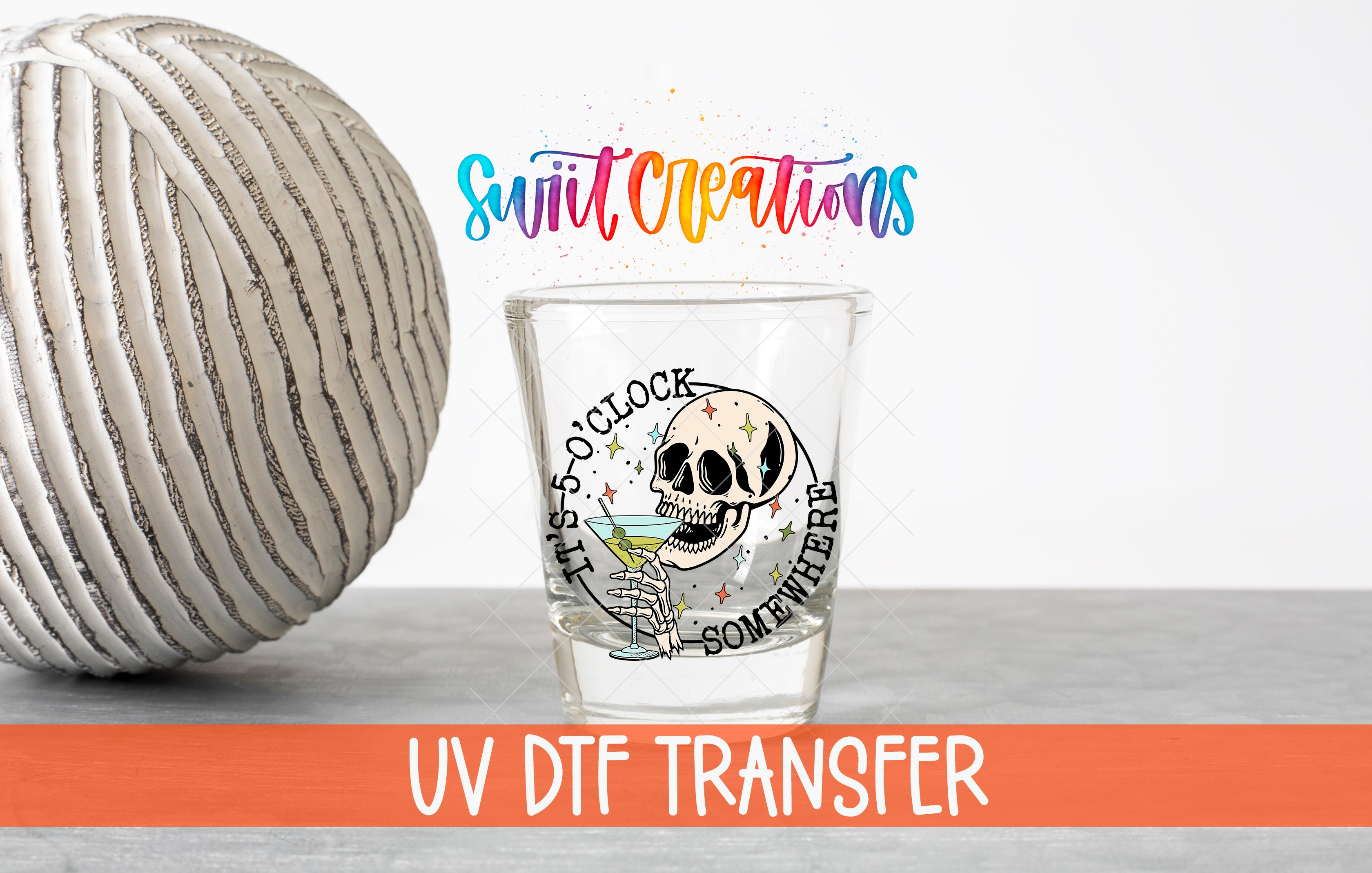 a glass with a skull design and the text "UV DFT Transfer" written on it, along with a striped ball and a colorful background.