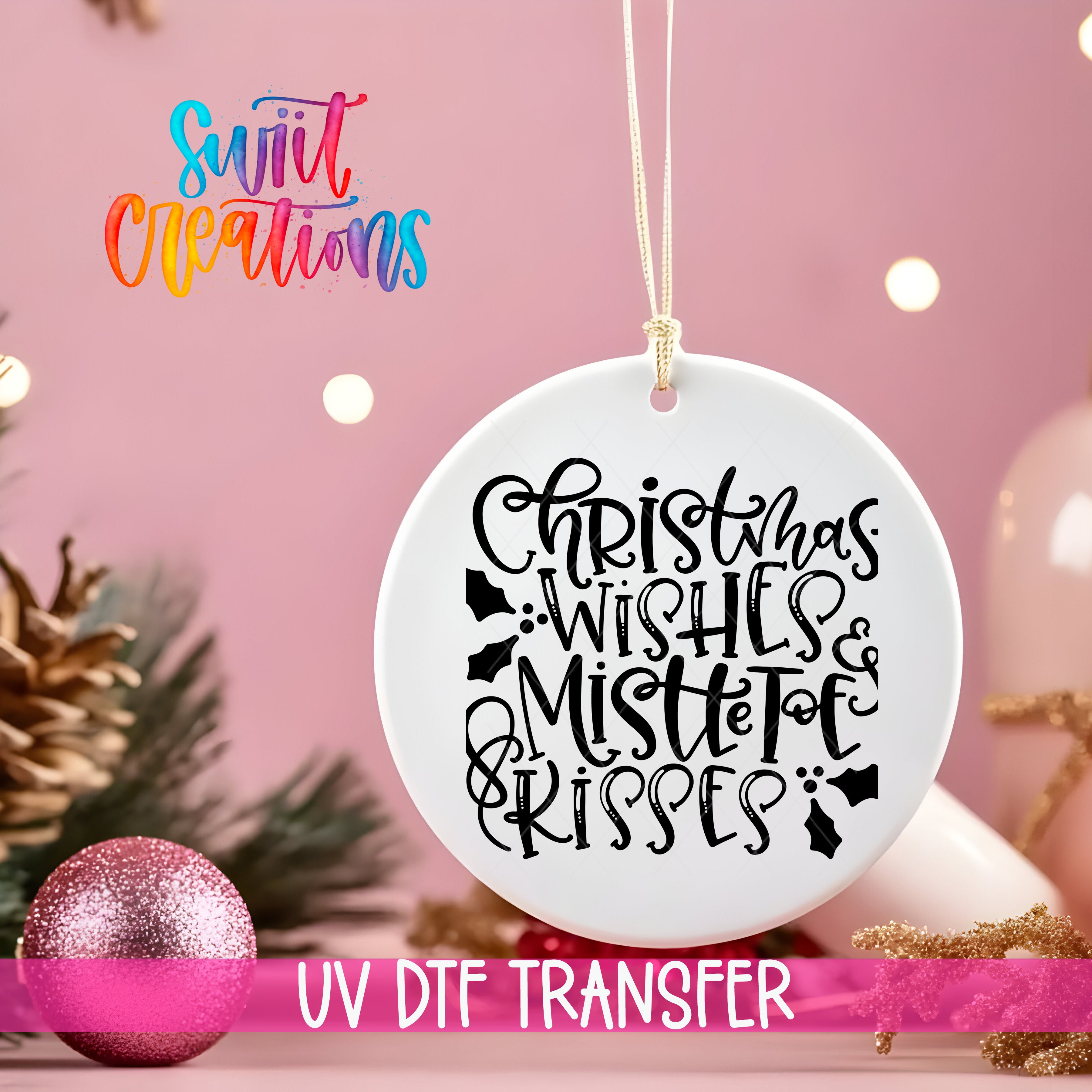 A white ornament with a black text design hangs on a string against a pink background, with Christmas decorations and a pink glitter ornament visible in the background.