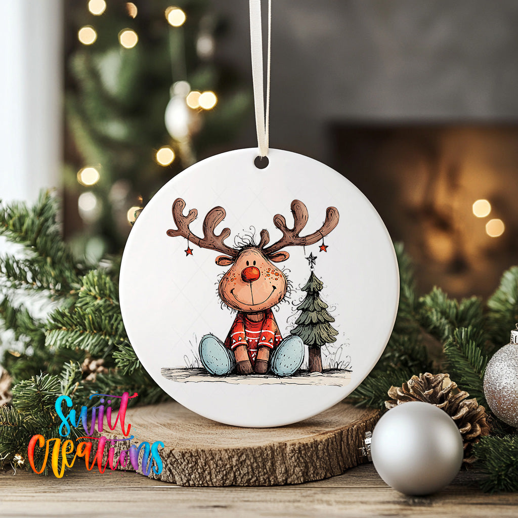 A white ceramic ornament featuring a cartoon reindeer sitting on a log, surrounded by Christmas decorations such as pine cones and ornaments.