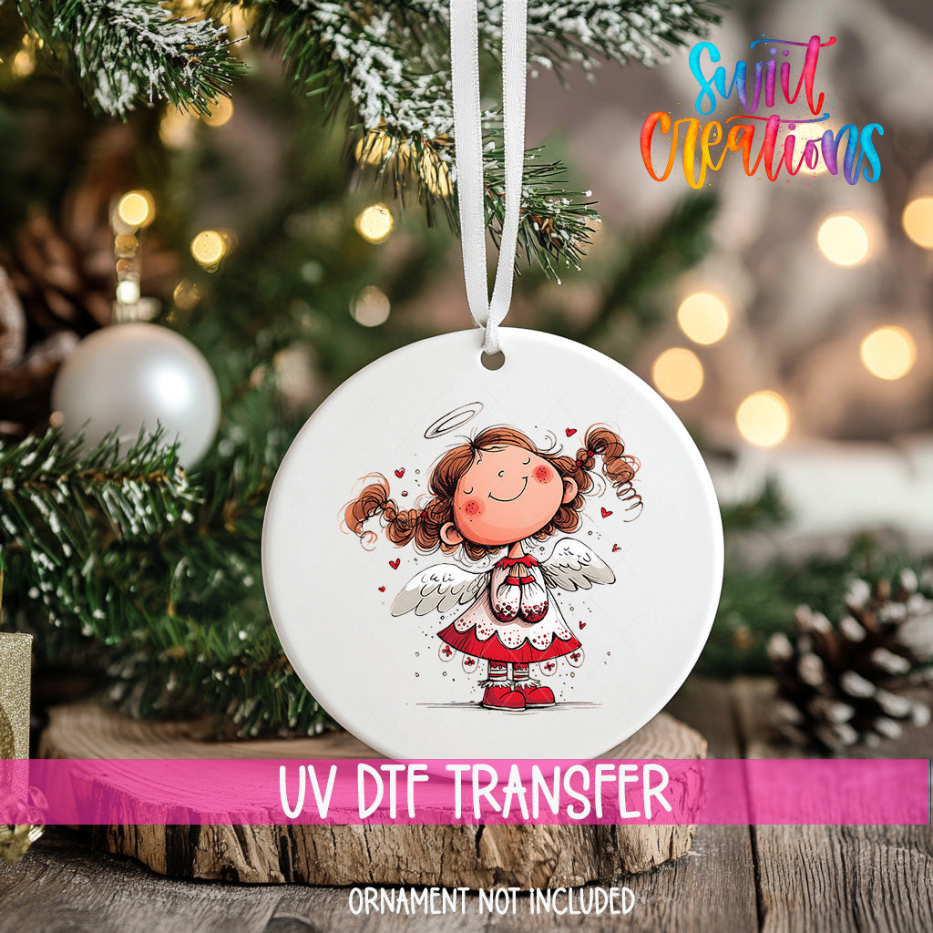 A white ceramic ornament with a smiling cartoon girl with curly hair and wings, hanging on a Christmas tree.