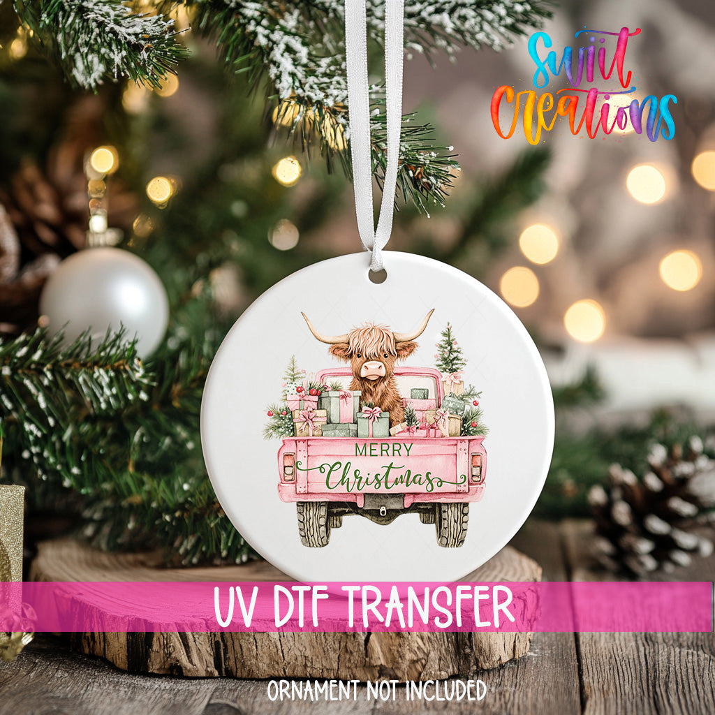 A Christmas ornament featuring a cow with horns, sitting in the bed of a pink truck, is hanging on a tree.