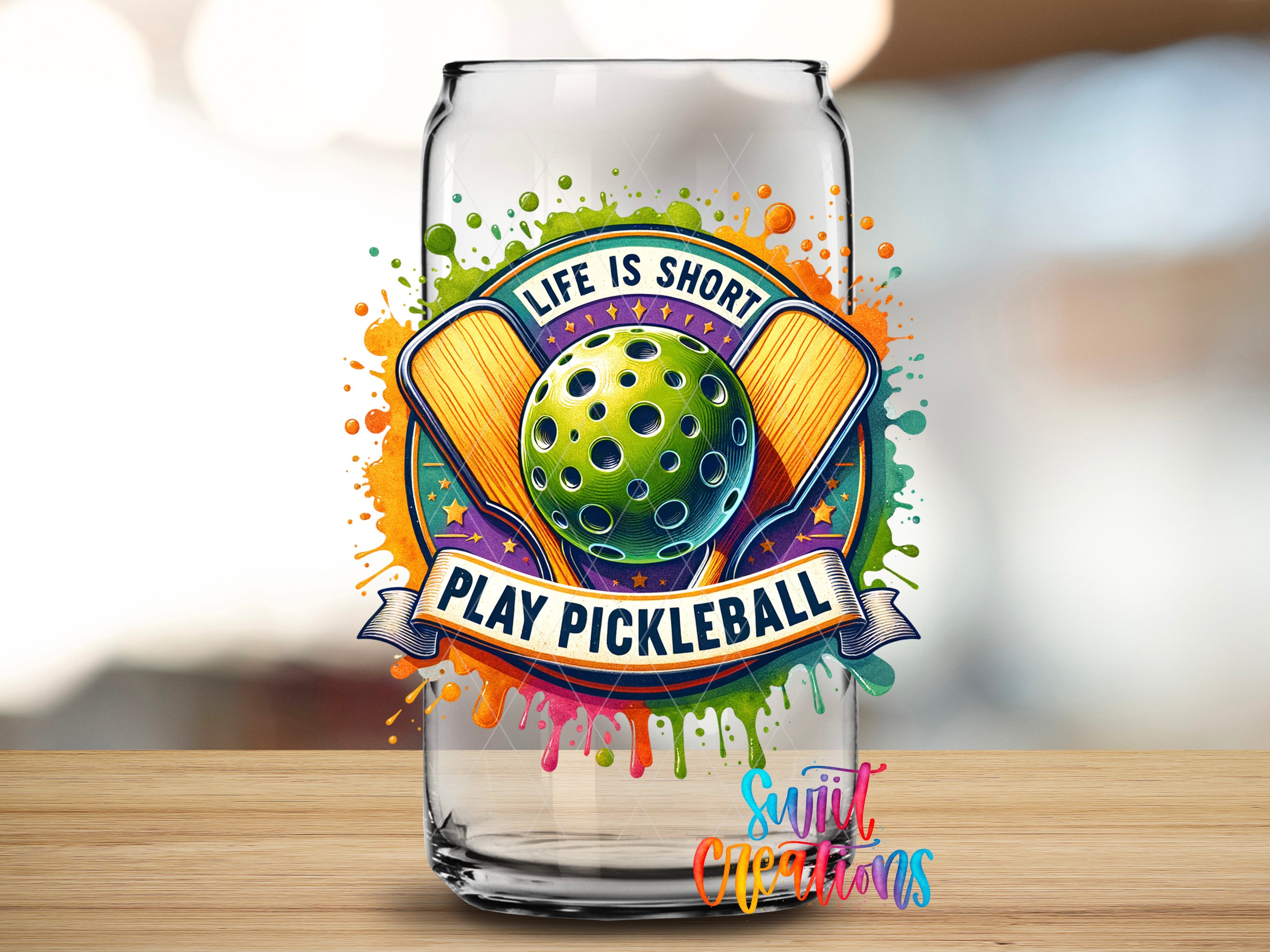 a glass can with a colorful and vibrant design, including a tennis racket, a ball, and a banner that says "Life is short, play pickleball".