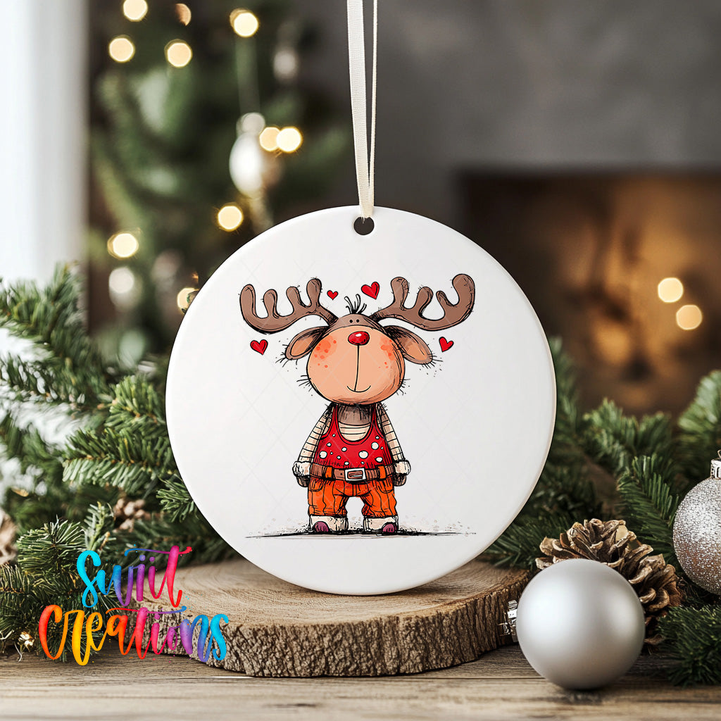 A white ornament featuring a cartoon reindeer with antlers and hearts, placed on a wooden surface with Christmas decorations in the background.