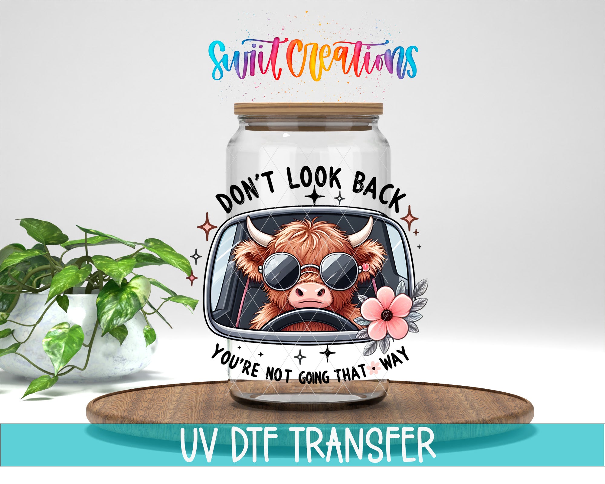 a glass jar with a cartoon cow wearing sunglasses and a flower, along with the text "DON'T LOOK BACK YOU'RE NOT GOING THAT WAY" printed on it. The jar is placed on a wooden surface, and there is a potted plant in the background.