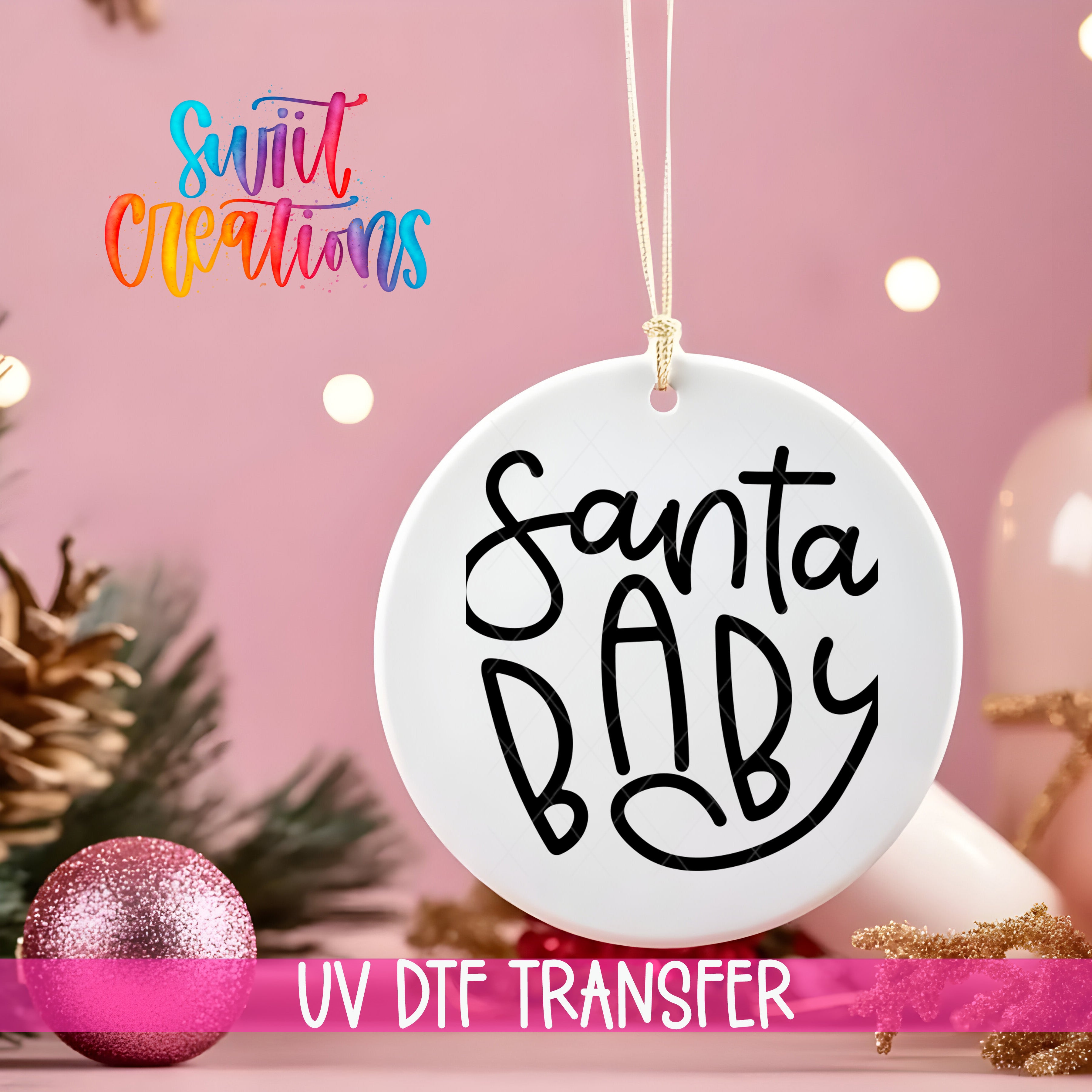 A white ornament with the text "Santa Baby" written on it, hanging against a pink background with Christmas decorations and lights visible in the background.