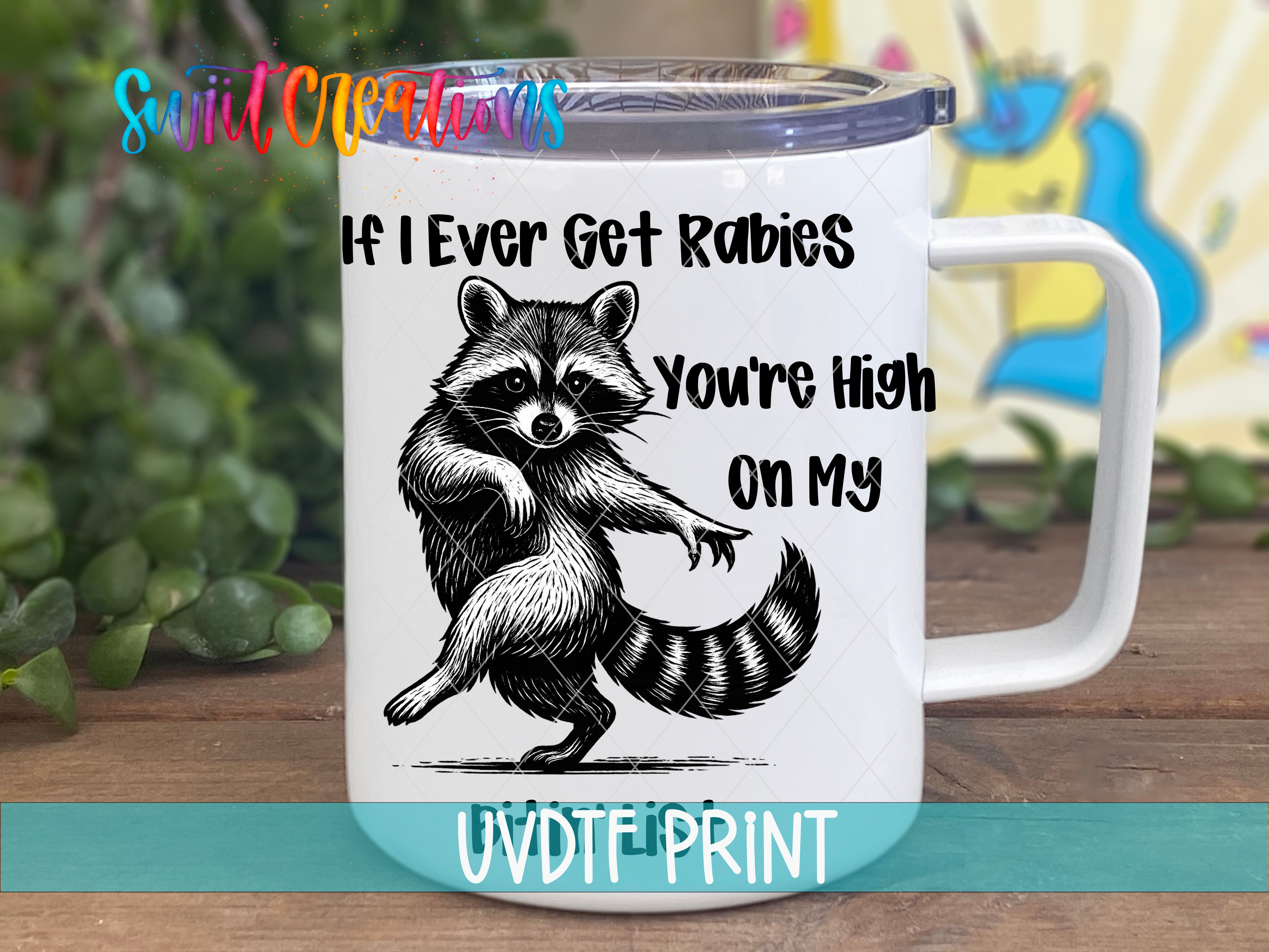 A white mug with a raccoon illustration and text on it, placed on a wooden surface.