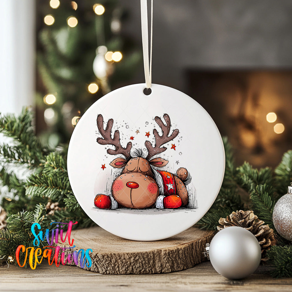 A white ceramic ornament featuring a cartoon reindeer with antlers and a starry background, surrounded by Christmas decorations and greenery.