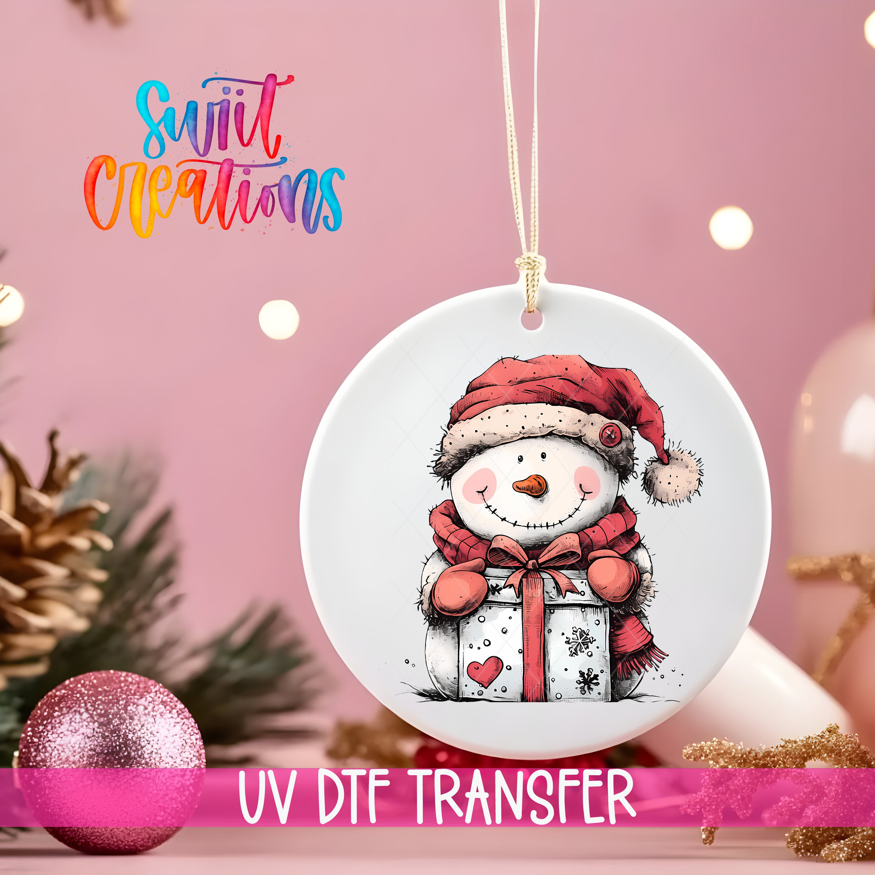A white ornament with a snowman and a gift box, hanging on a string against a pink background with Christmas decorations in the background.