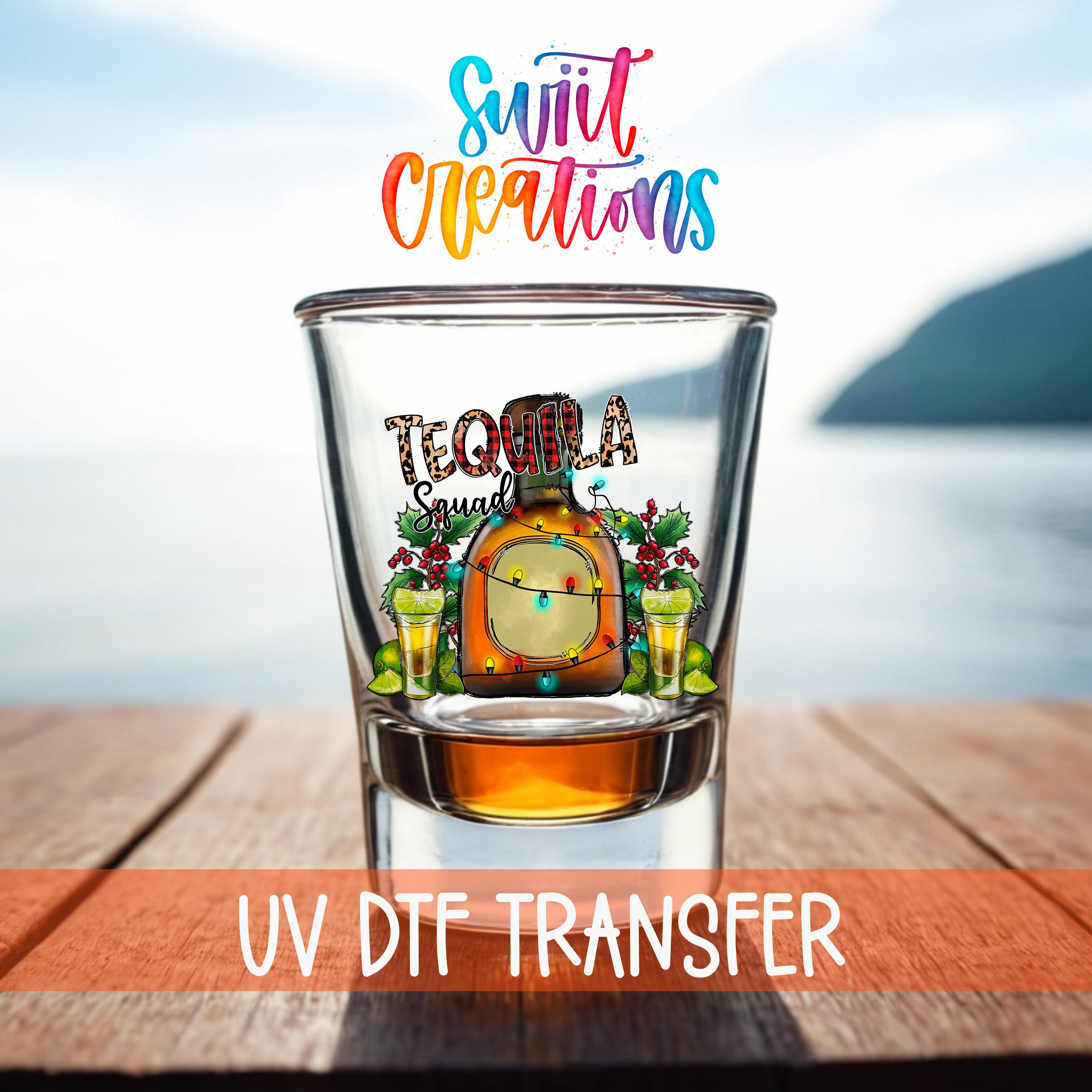 A glass of tequila with a colorful design and text, placed on a wooden surface with a body of water in the background.