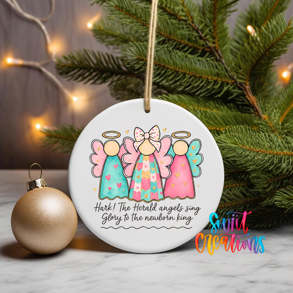 A white ceramic ornament with a Christmas tree in the background, featuring three colorful angel figures and the text "Hark! The Herald angels sing glory to the newborn king".