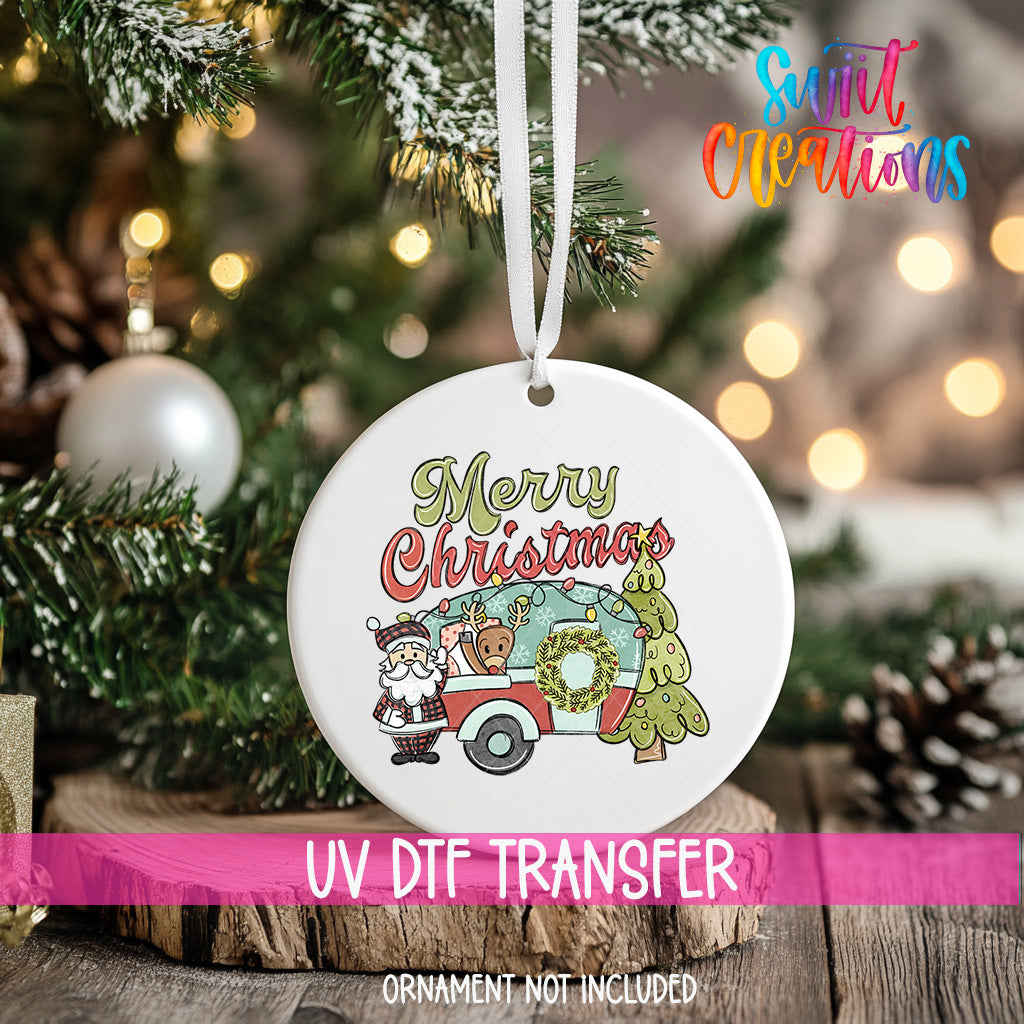 A white Christmas ornament with a Santa Claus and a camper van design hangs on a Christmas tree.