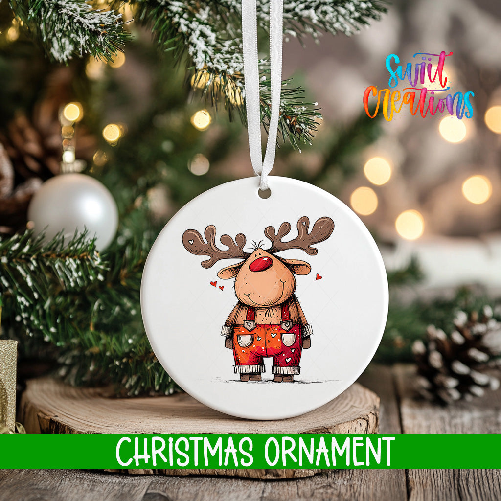 A white Christmas ornament featuring a cartoon reindeer with antlers and a red nose, hanging on a tree branch.