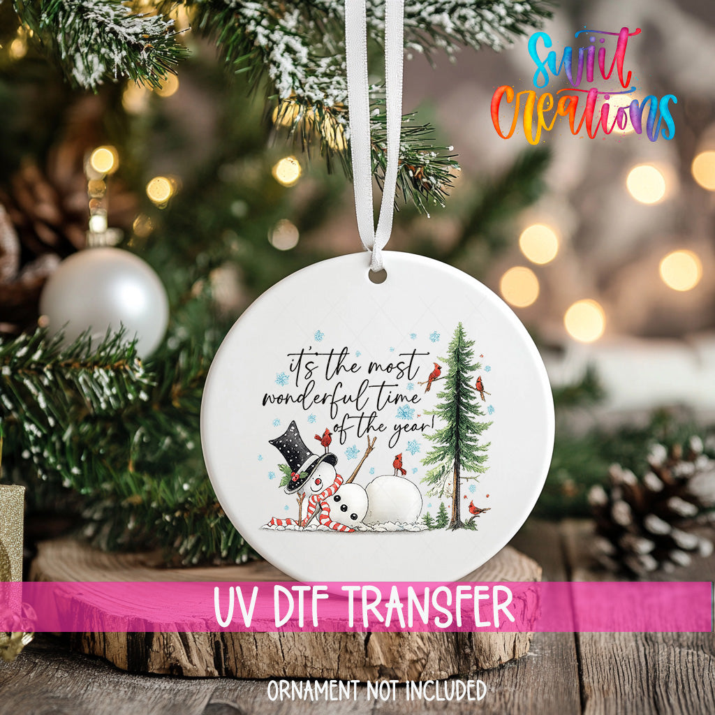 A white ceramic ornament with a snowman and Christmas tree design hangs on a Christmas tree.