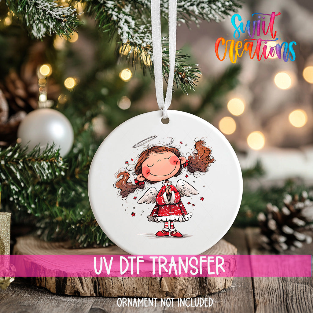 A white ornament with a cartoon illustration of a smiling girl with wings is hanging on a Christmas tree.