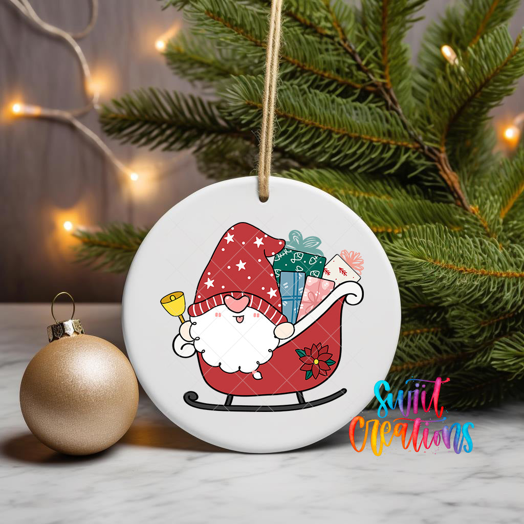 A white ornament with a gnome riding a sled carrying presents is displayed on a table, with a Christmas tree and twinkling lights in the background.