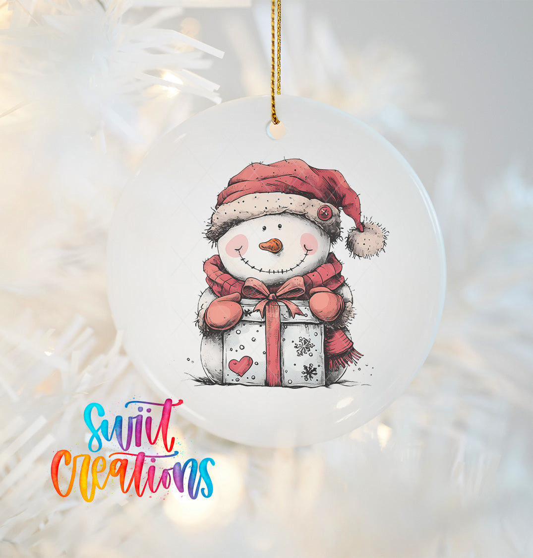 A white ornament with a snowman figure wearing a red hat and scarf, holding a gift box, hanging on a string.