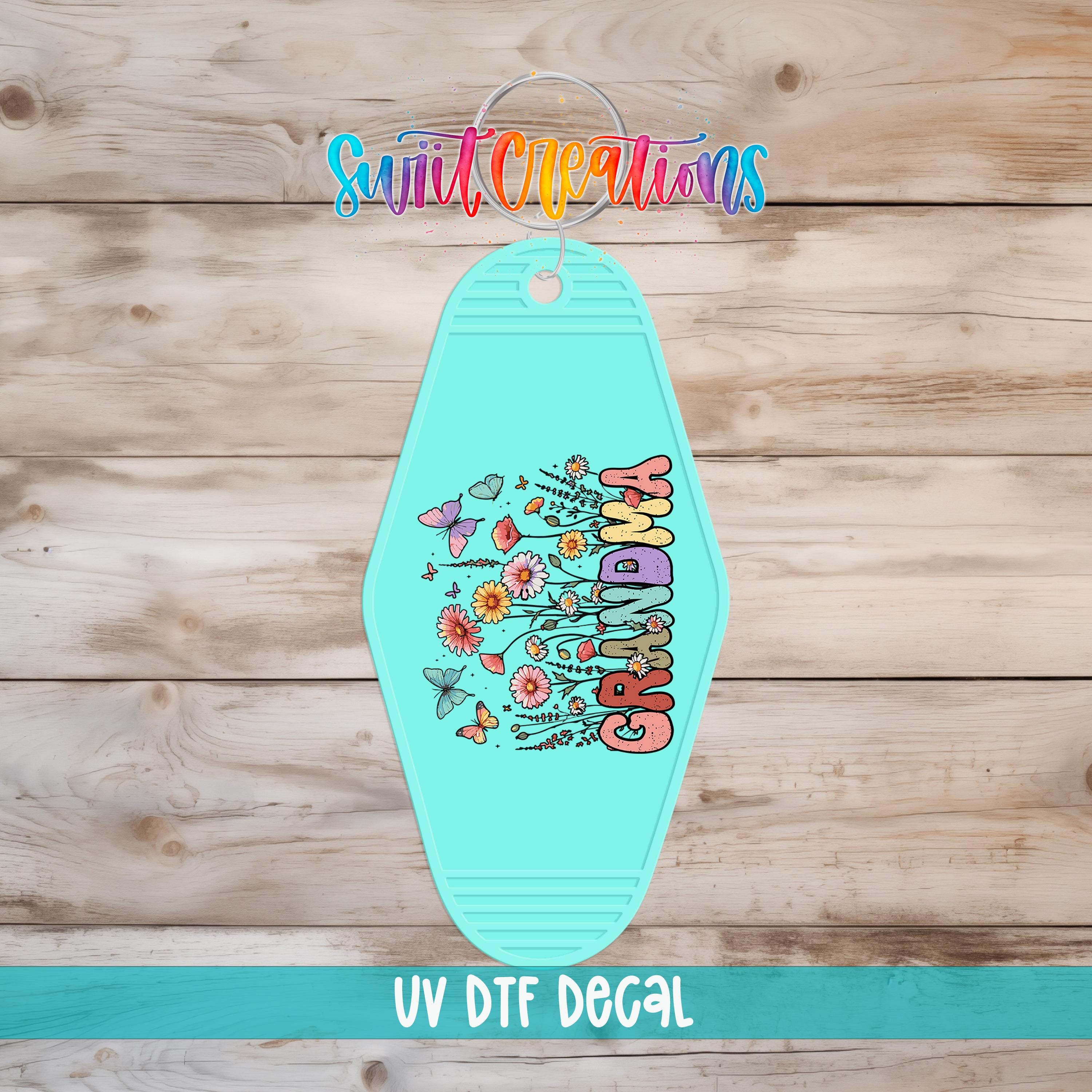 A turquoise keychain with a colorful floral design and the text "GRANDMA" printed on it, placed on a wooden surface.