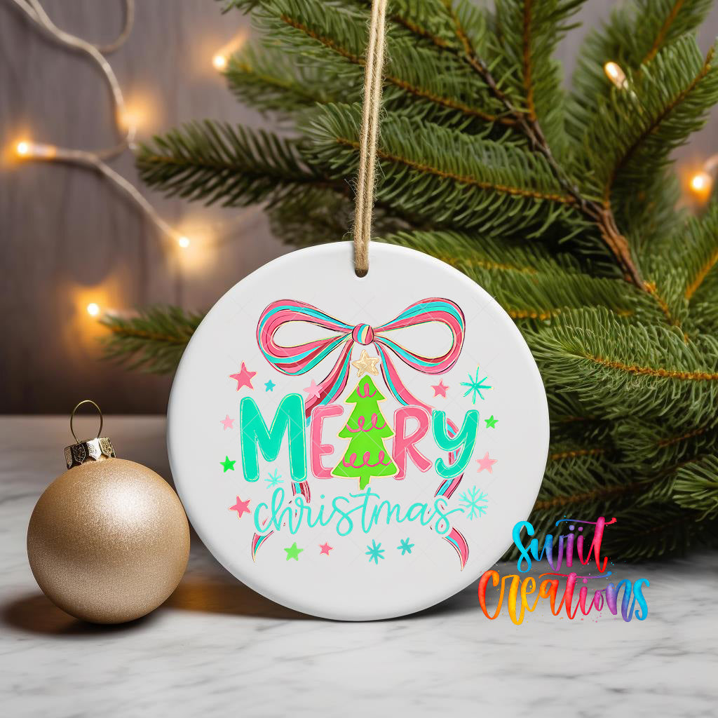 A white Christmas ornament with the text "Merry Christmas" and colorful decorations is displayed on a table, with a gold ornament and a pine tree in the background.