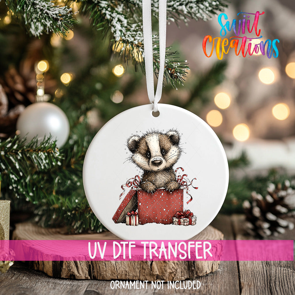 A white ornament with a cartoon badger sitting inside a red gift box, hanging on a Christmas tree.