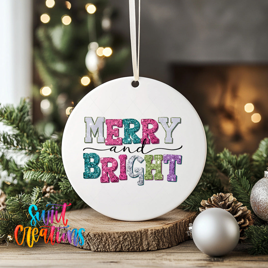 A white ceramic ornament with the text "MERRY AND BRIGHT" in colorful letters, hanging from a string. The ornament is placed on a wooden surface, surrounded by Christmas decorations such as pine cones and ornaments.