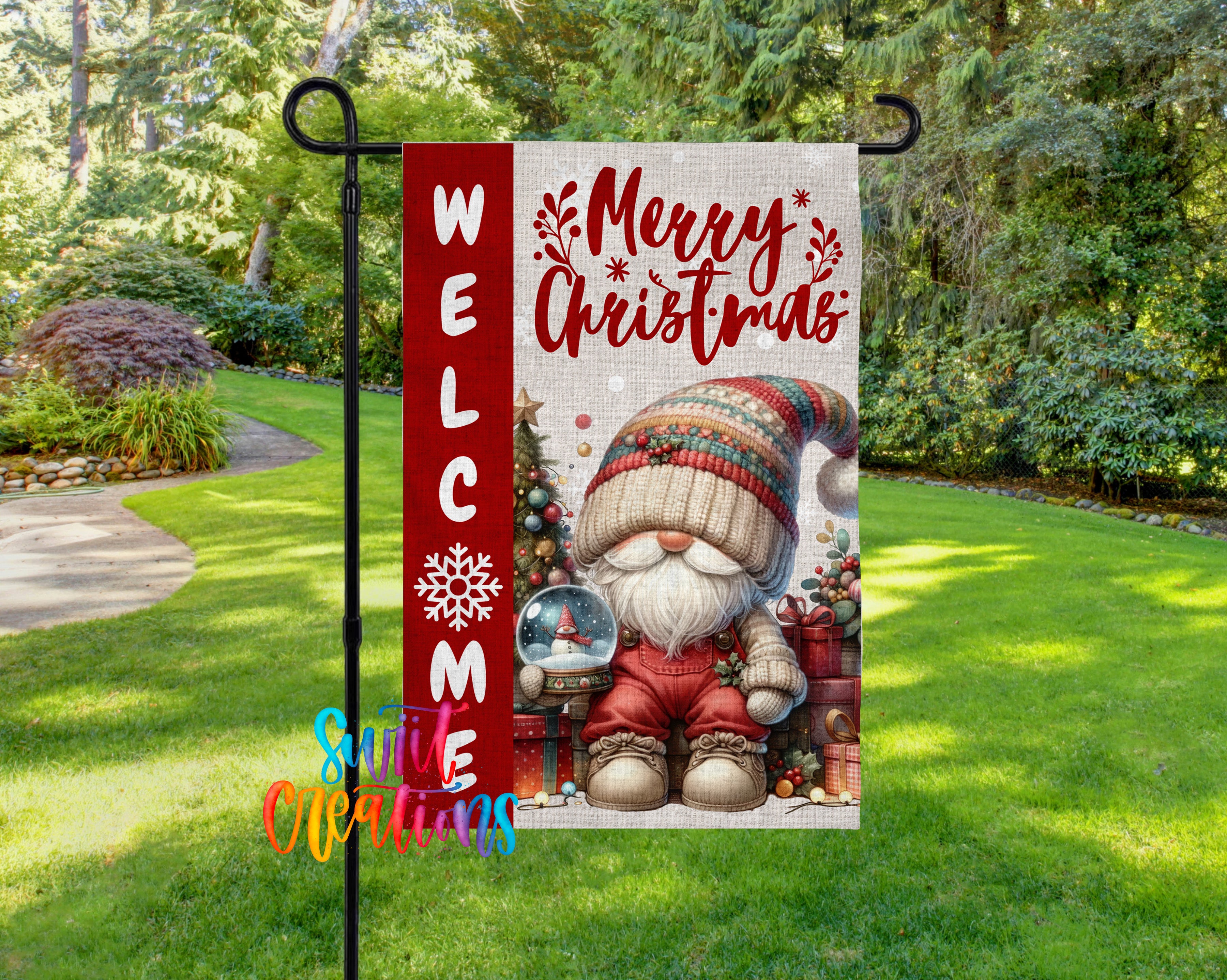 A red and white welcome sign with a gnome holding a snow globe, surrounded by Christmas decorations, is displayed in a garden setting.