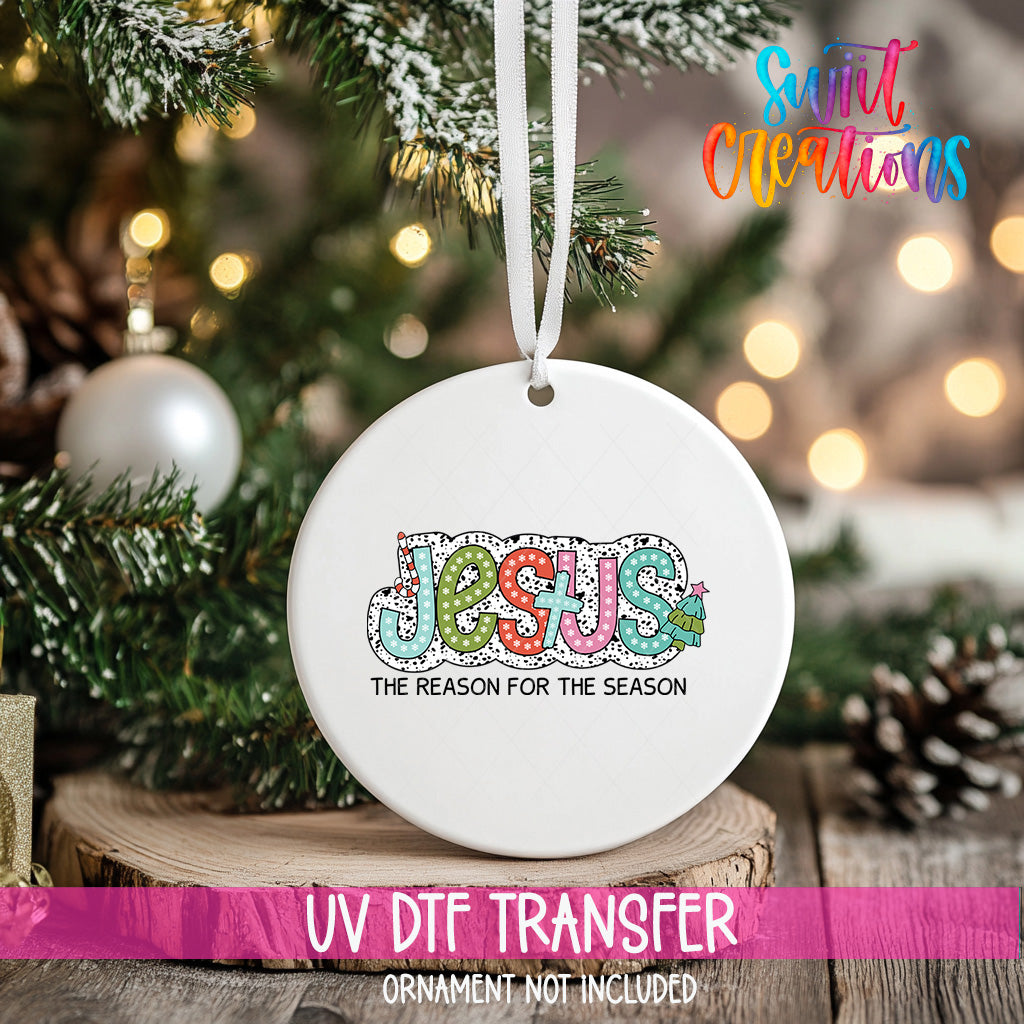 A white Christmas ornament with the word "JESUS" and the phrase "THE REASON FOR THE SEASON" printed on it, hanging on a tree.