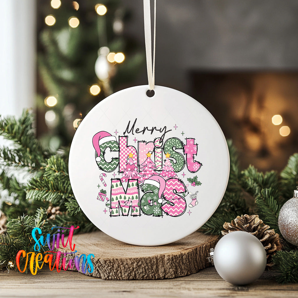 A white Christmas ornament with the text "Merry Christmas" in a colorful, festive font is displayed on a wooden surface, surrounded by pine branches and other holiday decorations.