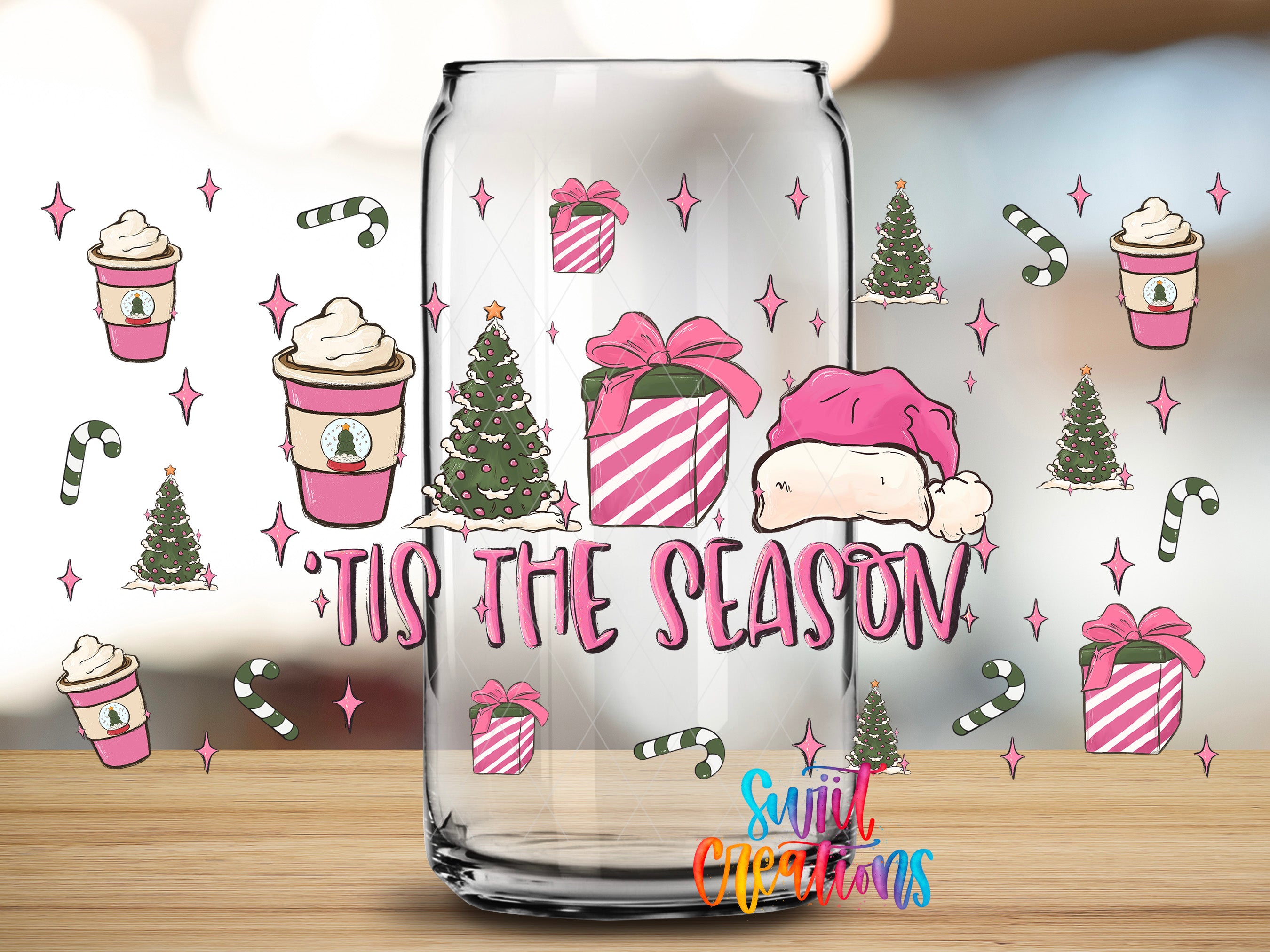 A glass can with a festive design featuring Christmas trees, gift boxes, and a Santa hat, along with the text "Tis the Season" and "Sunlit Occasions" printed on it.